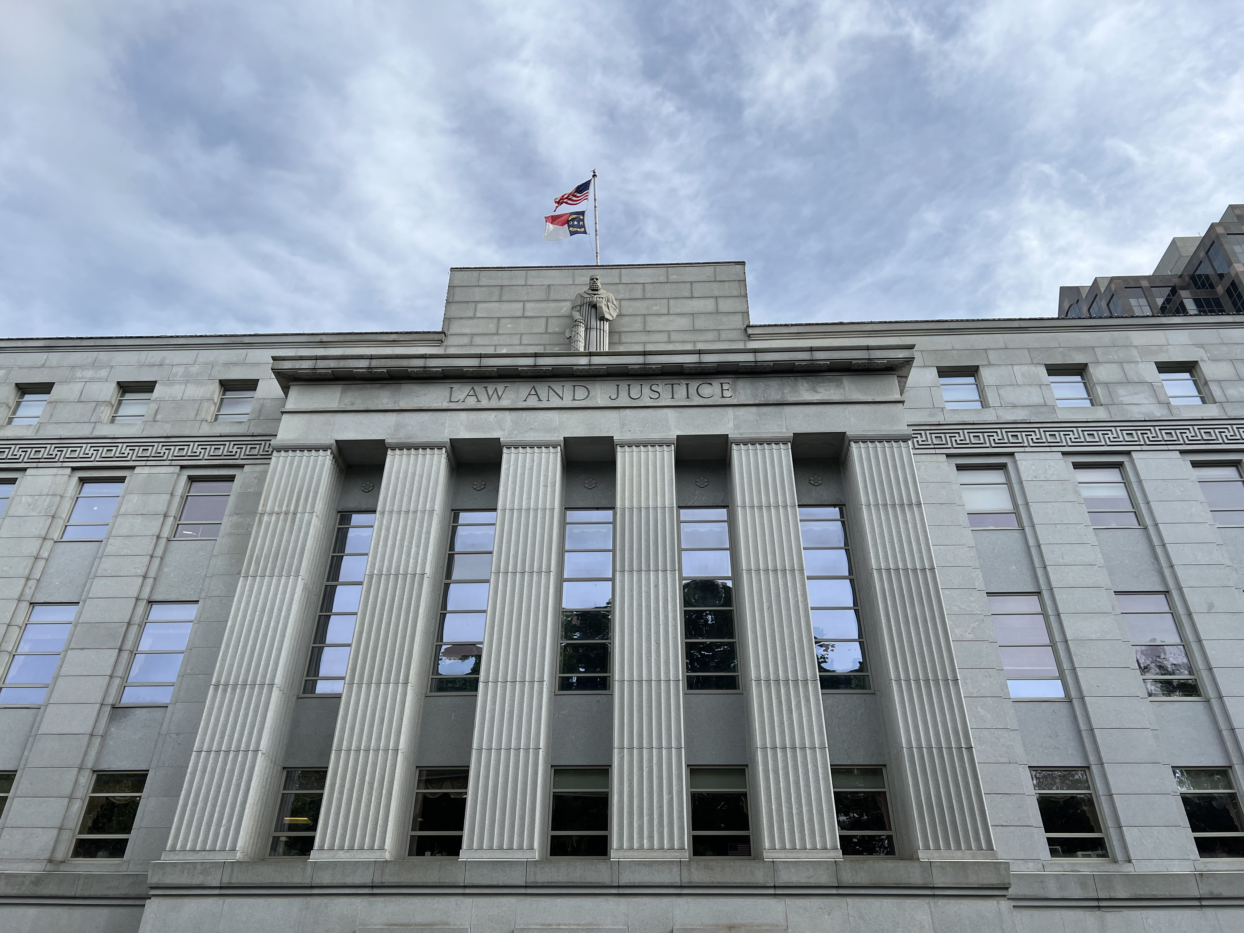 The courthouse is shown at a looming angle with clouds swirling above. It is a pale-colored building with columns and the words "Law and Justice" inscribed on stone.