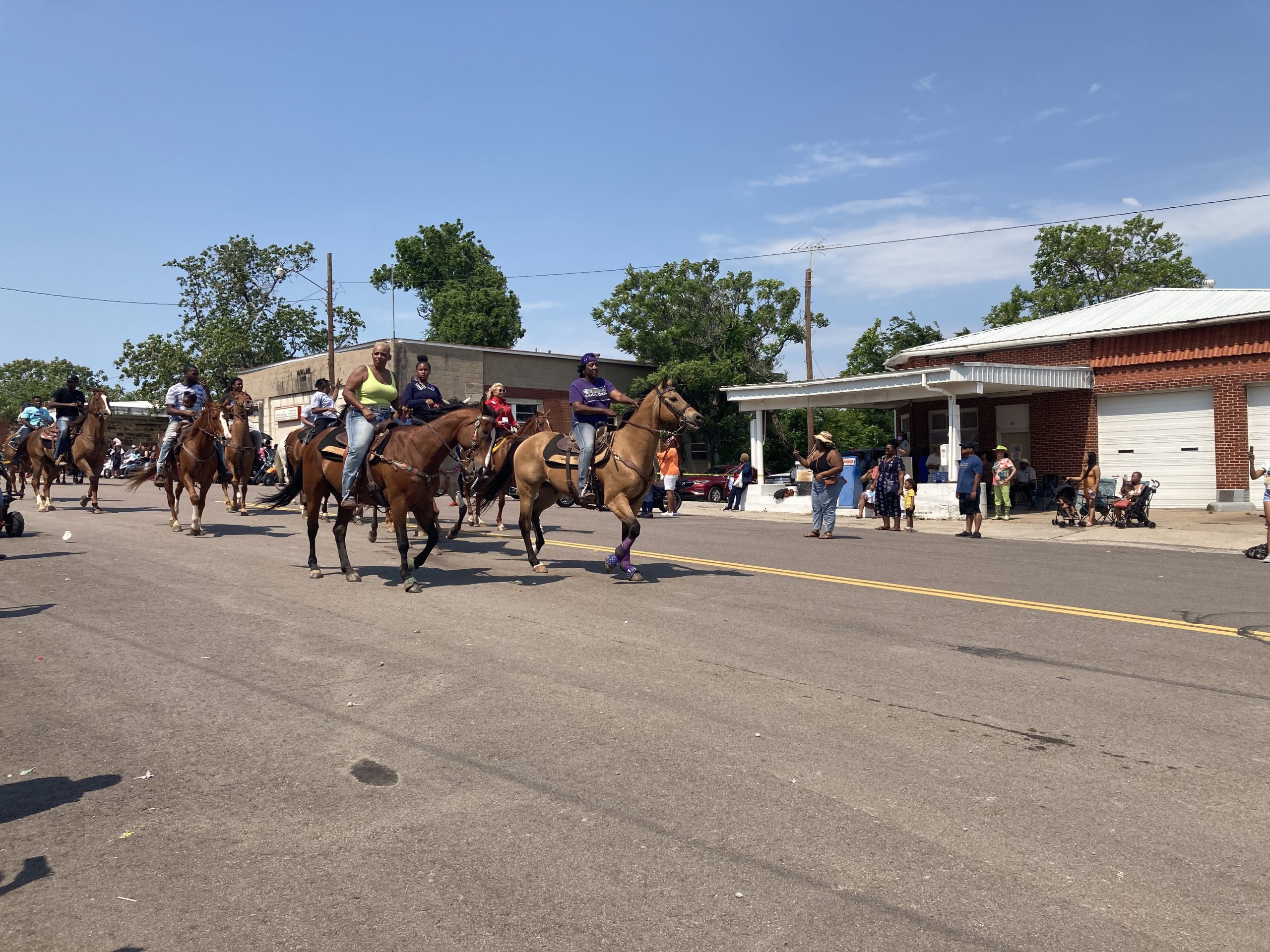 Riders on horse travel down the street as residents watch.