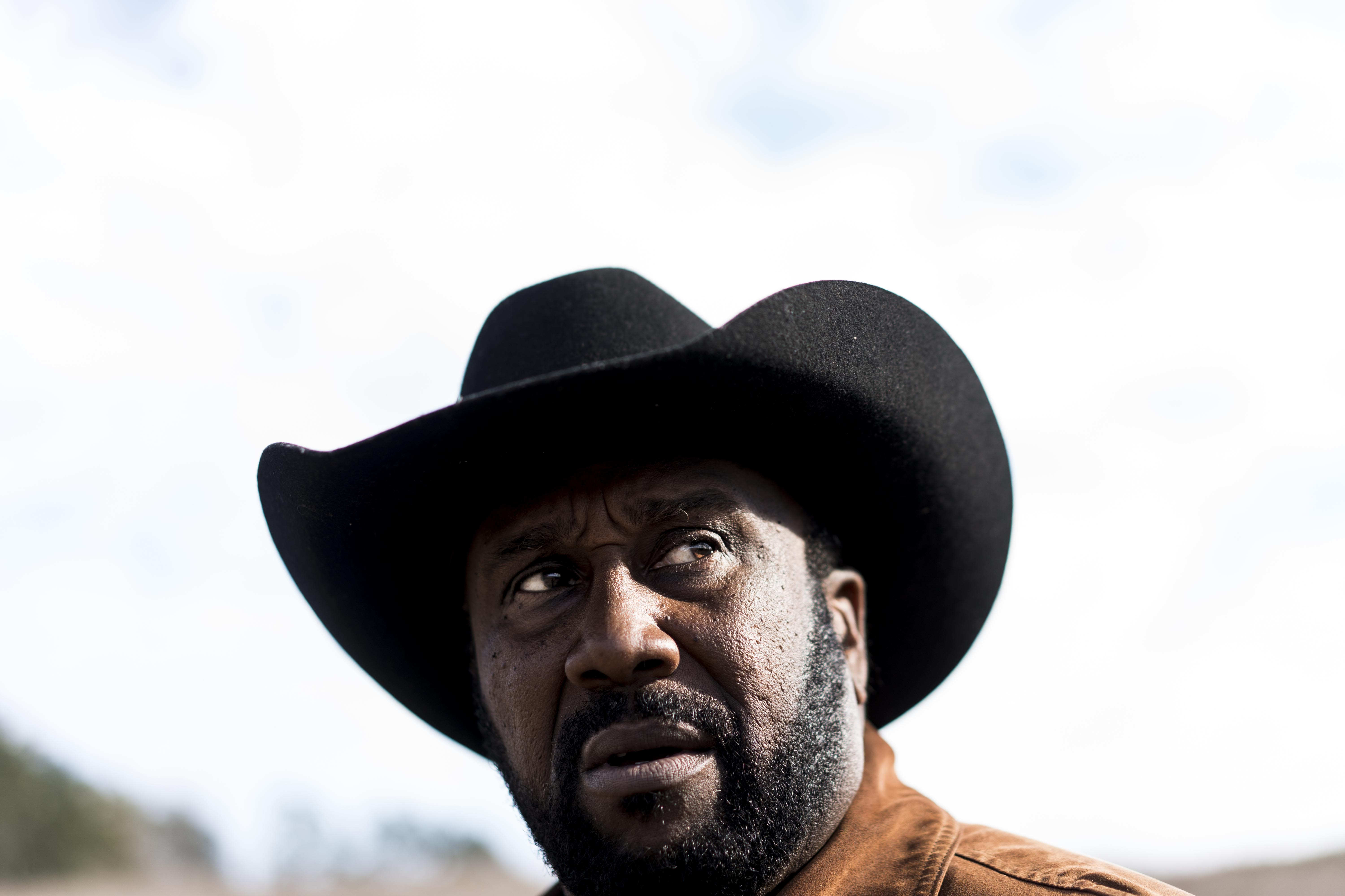 John Boyd looks out into the distance. He is wearing a brown jacket and black cowboy hat.