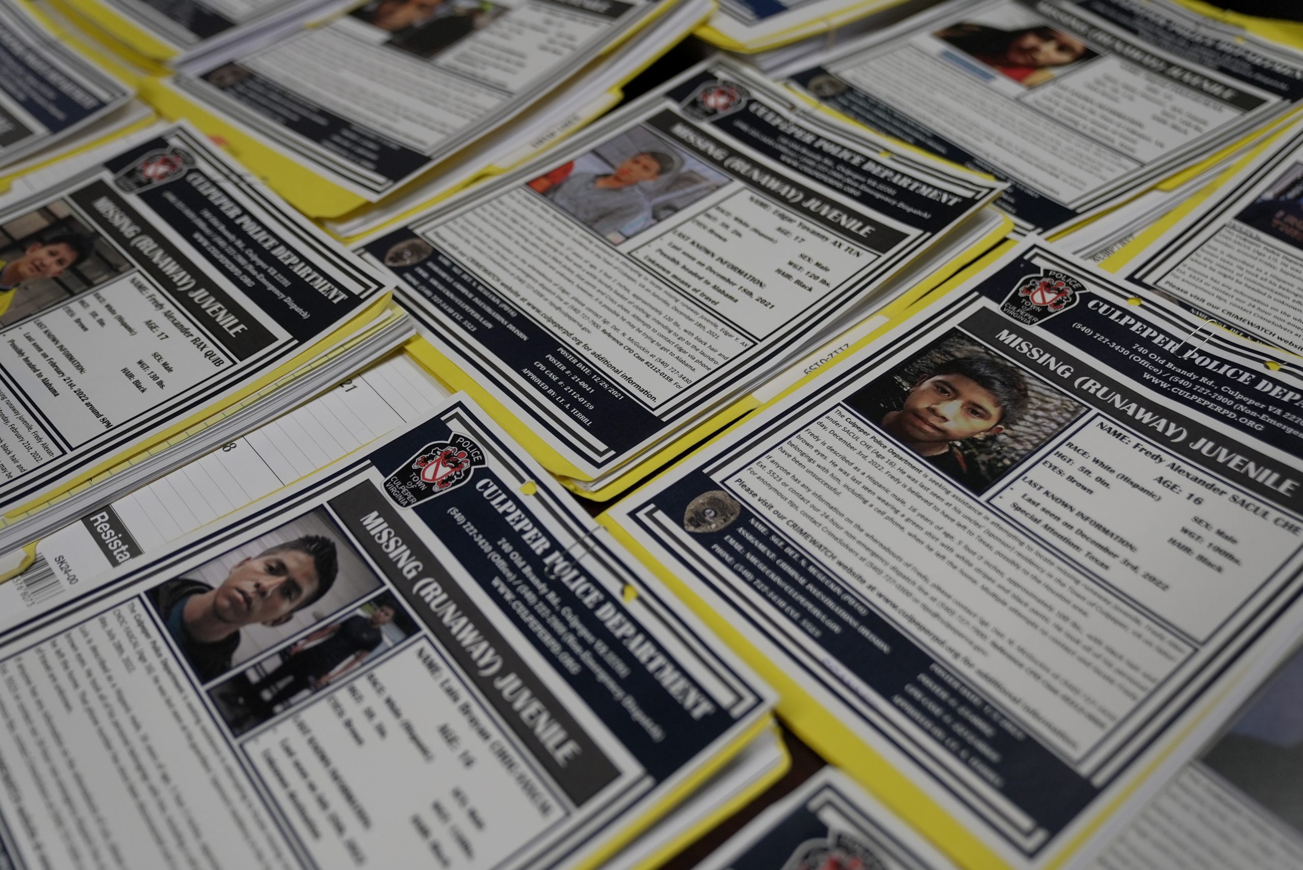 Several missing migrant children posters are displayed across a table.