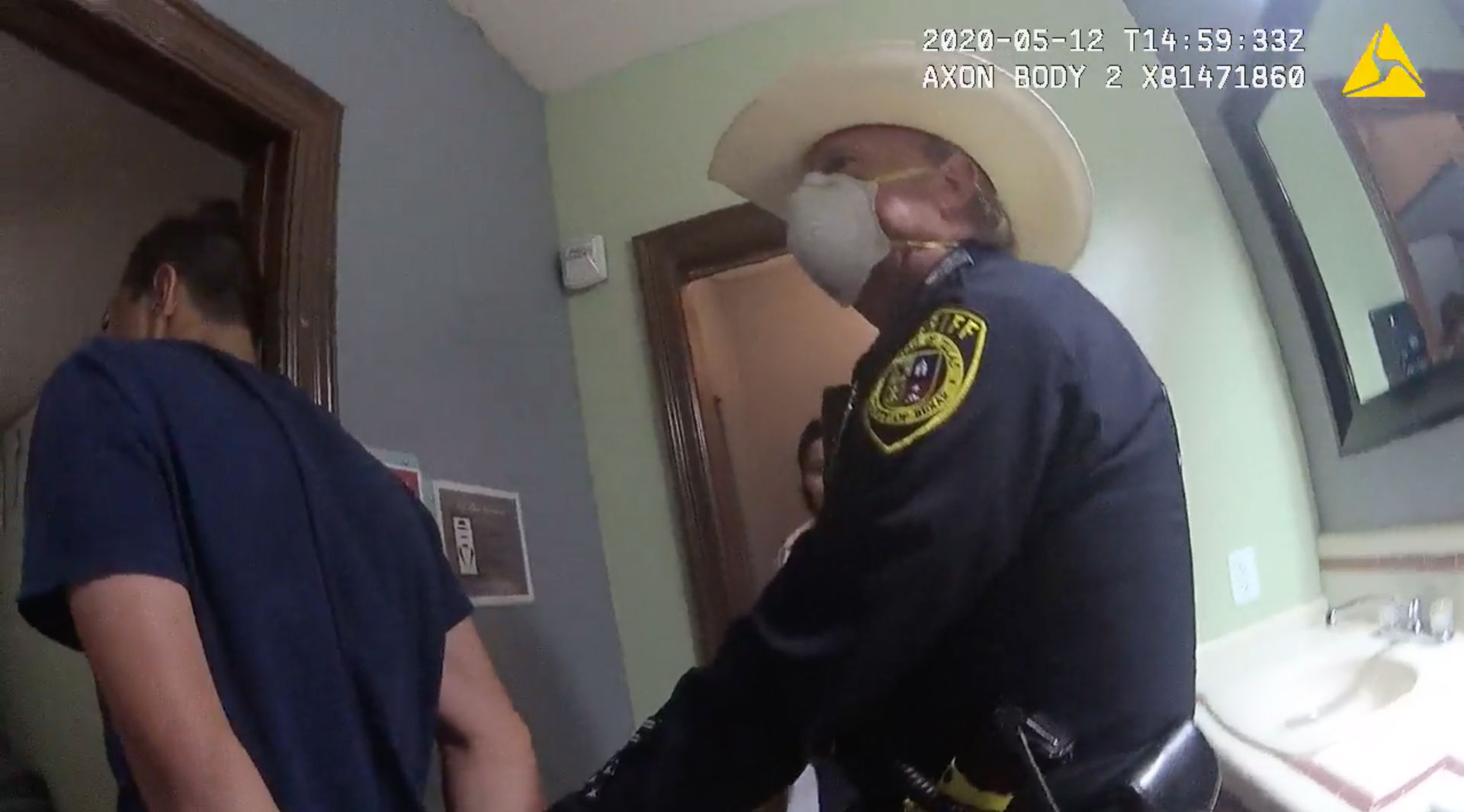 Bexar County Sheriff’s Deputy Harold Schneider leads a teenage boy out of a bathroom. The teen’s face is not visible, and his hands are behind his back.