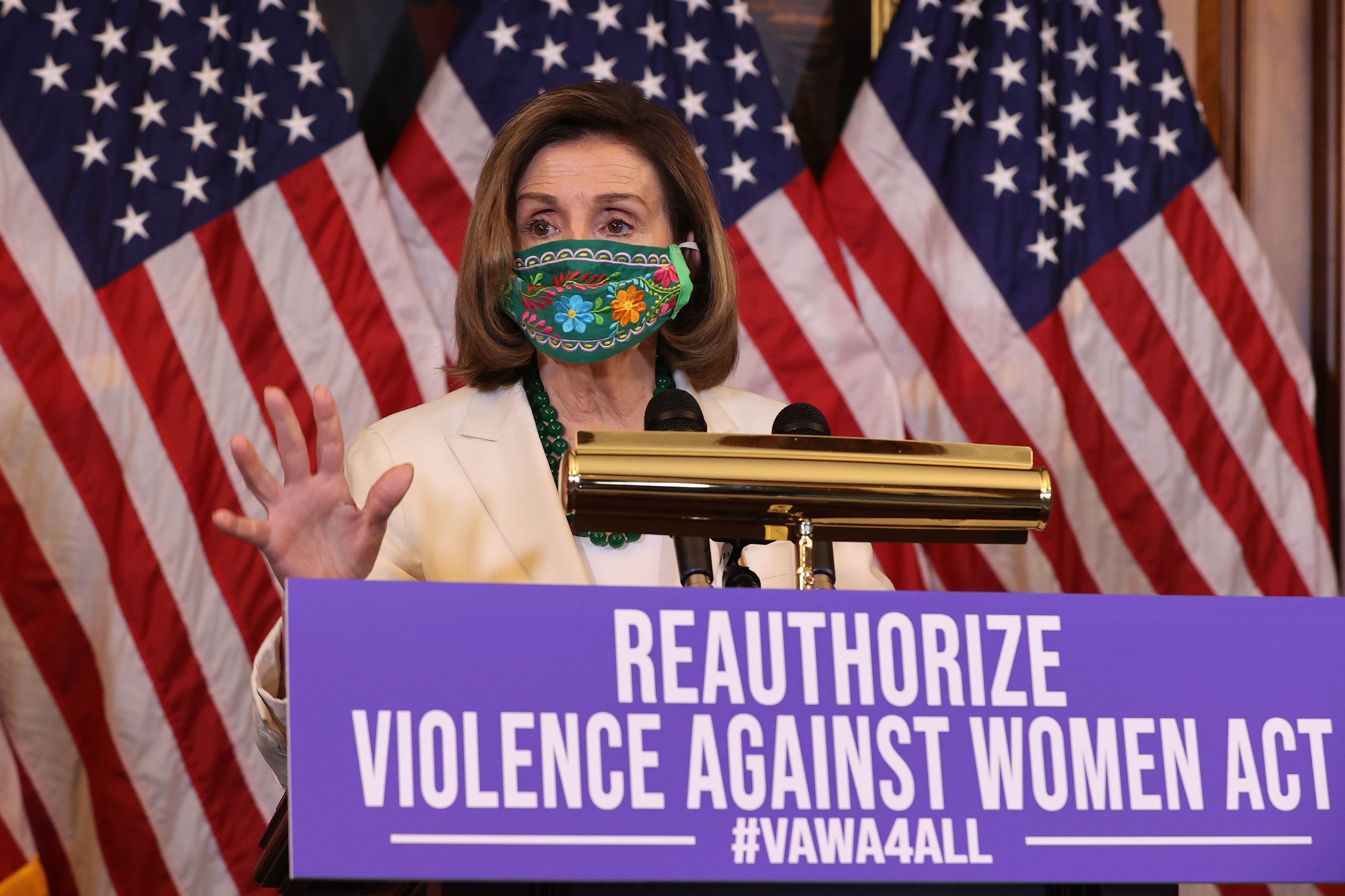 Nancy Pelosi stands behind a lectern. In front of her is a sign that says, “Reauthorize Violence Against Women Act.”