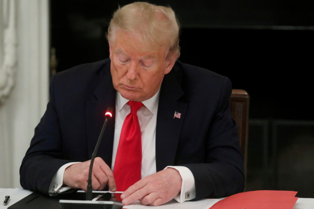 U.S. President Donald Trump is seen tapping the screen on a mobile phone during a roundtable discussion on the reopening o...