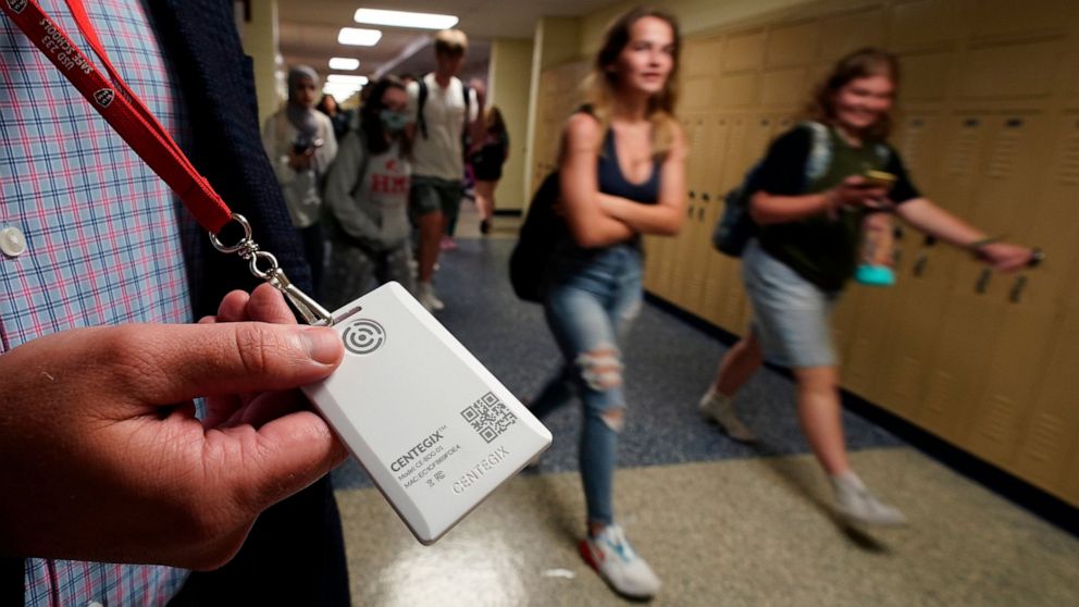 Brent Kiger, Olathe Public Schools' director of safety service, displays a panic-alert button while students at Olathe South High School rush between classes Friday, Aug. 19, 2022, in Olathe, Kan. The district introduced the buttons, which allow staf