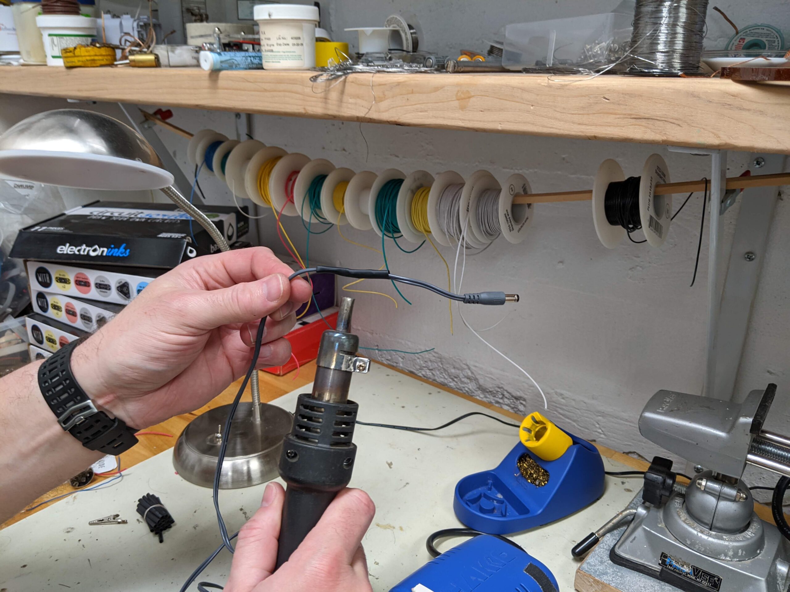 a pair of hands applying heat-shrink tubing to a cord using a heat gun