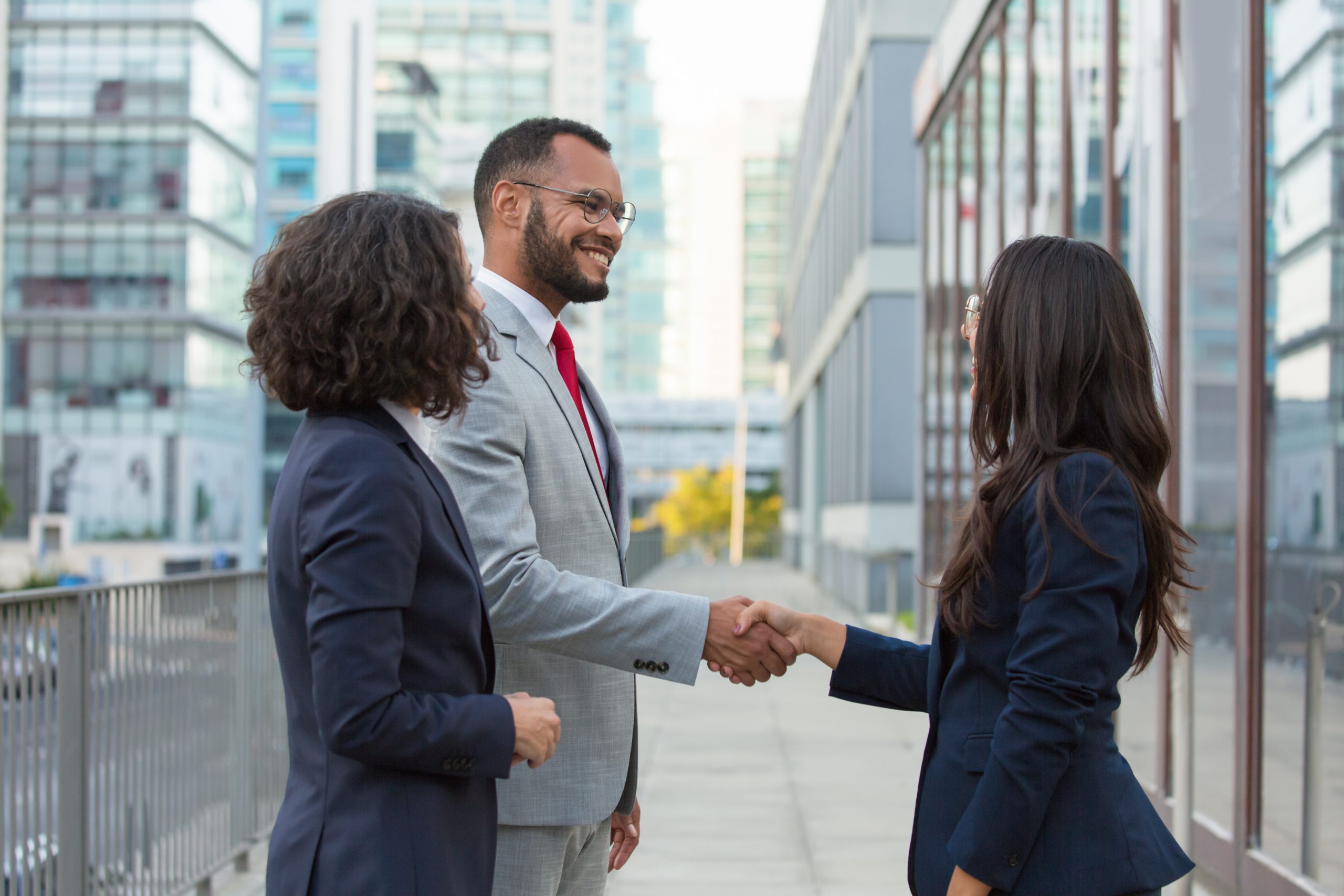 Happy positive business people meeting outside. Business man and women standing in city street, shaking hands, smiling and talking. Business communication concept