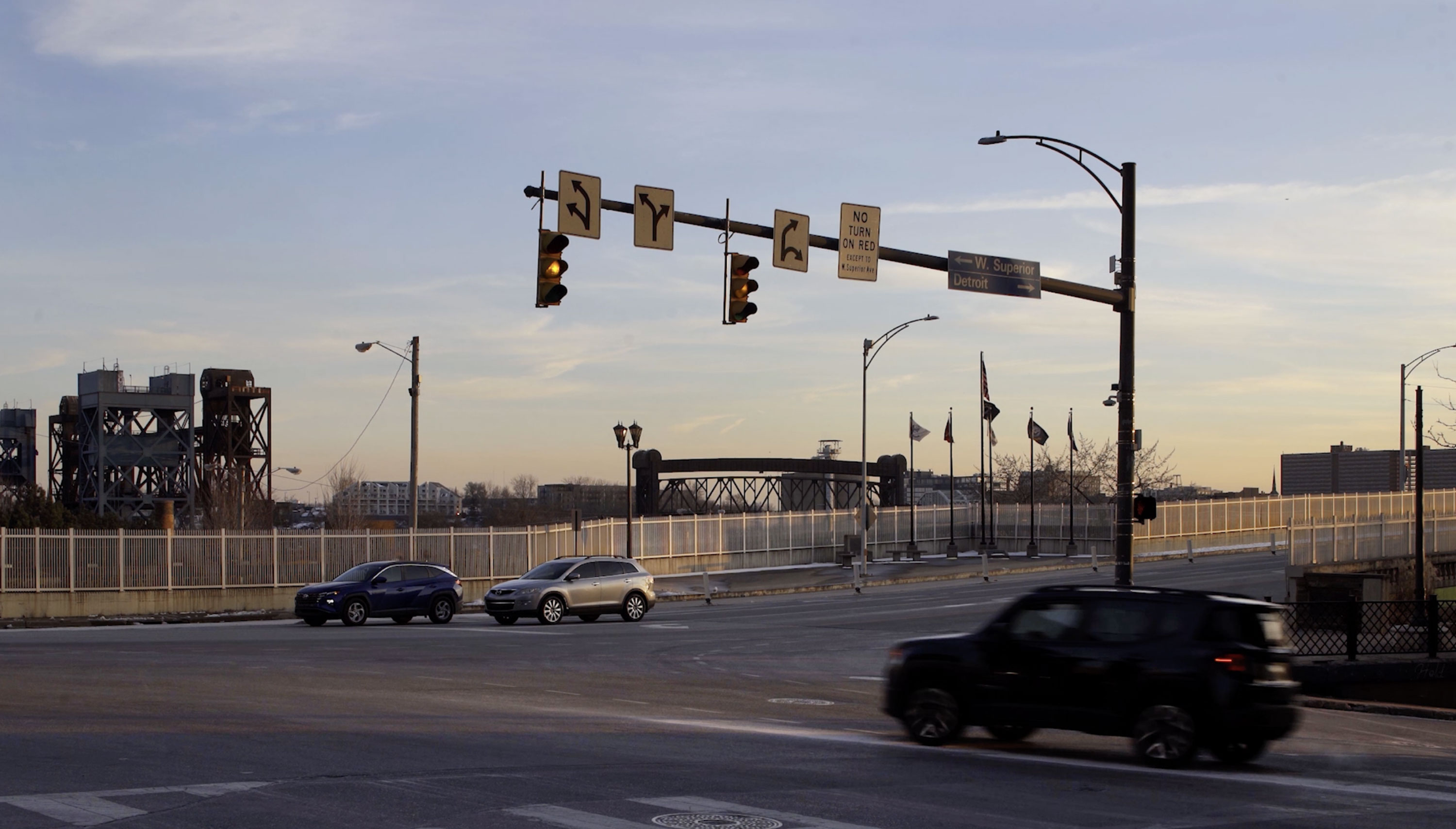 A photo shows cars driving through an intersection under changing stop lights. A surveillance camera is mounted on the stoplight pole.