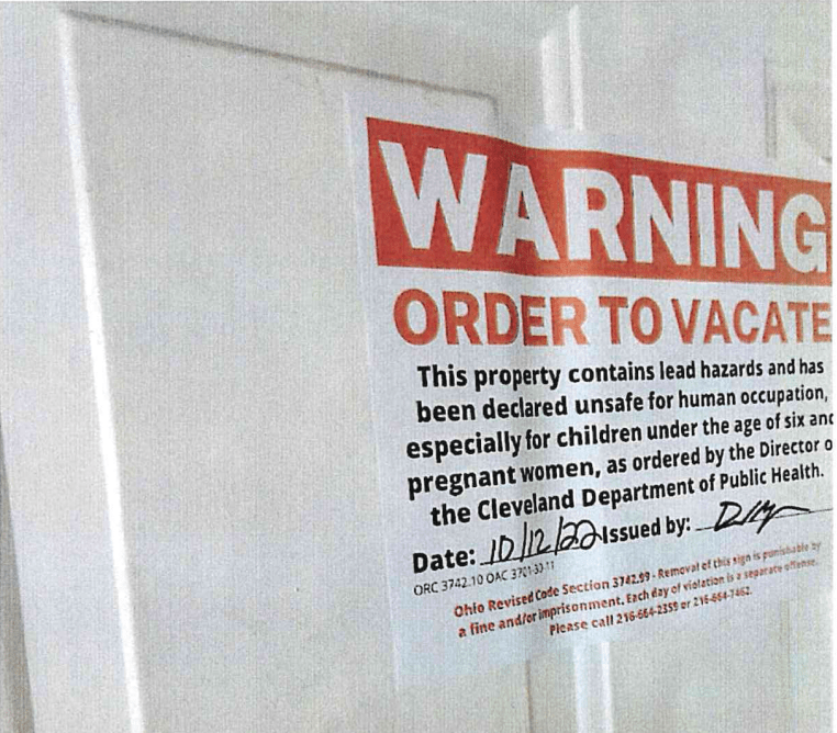 Warning sign posted on a door about lead poisoning hazards.