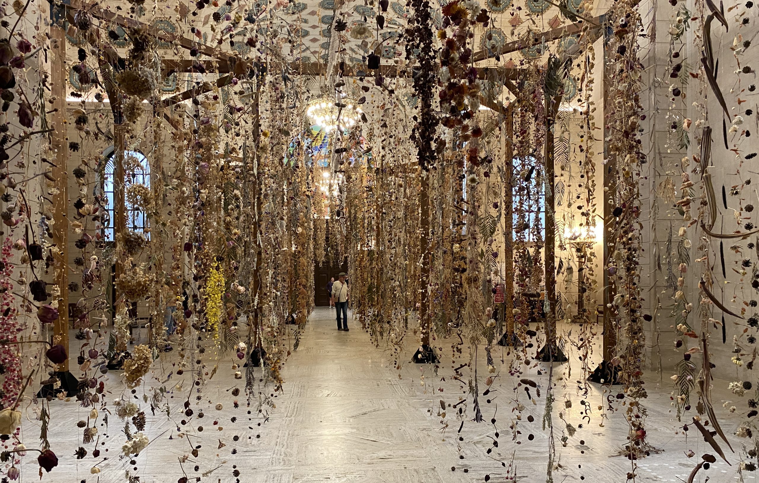 A man stands in the middle of walkway inside the main branch of the Cleveland Public Library surrounded by dried flowers hanging in strings from the ceiling.