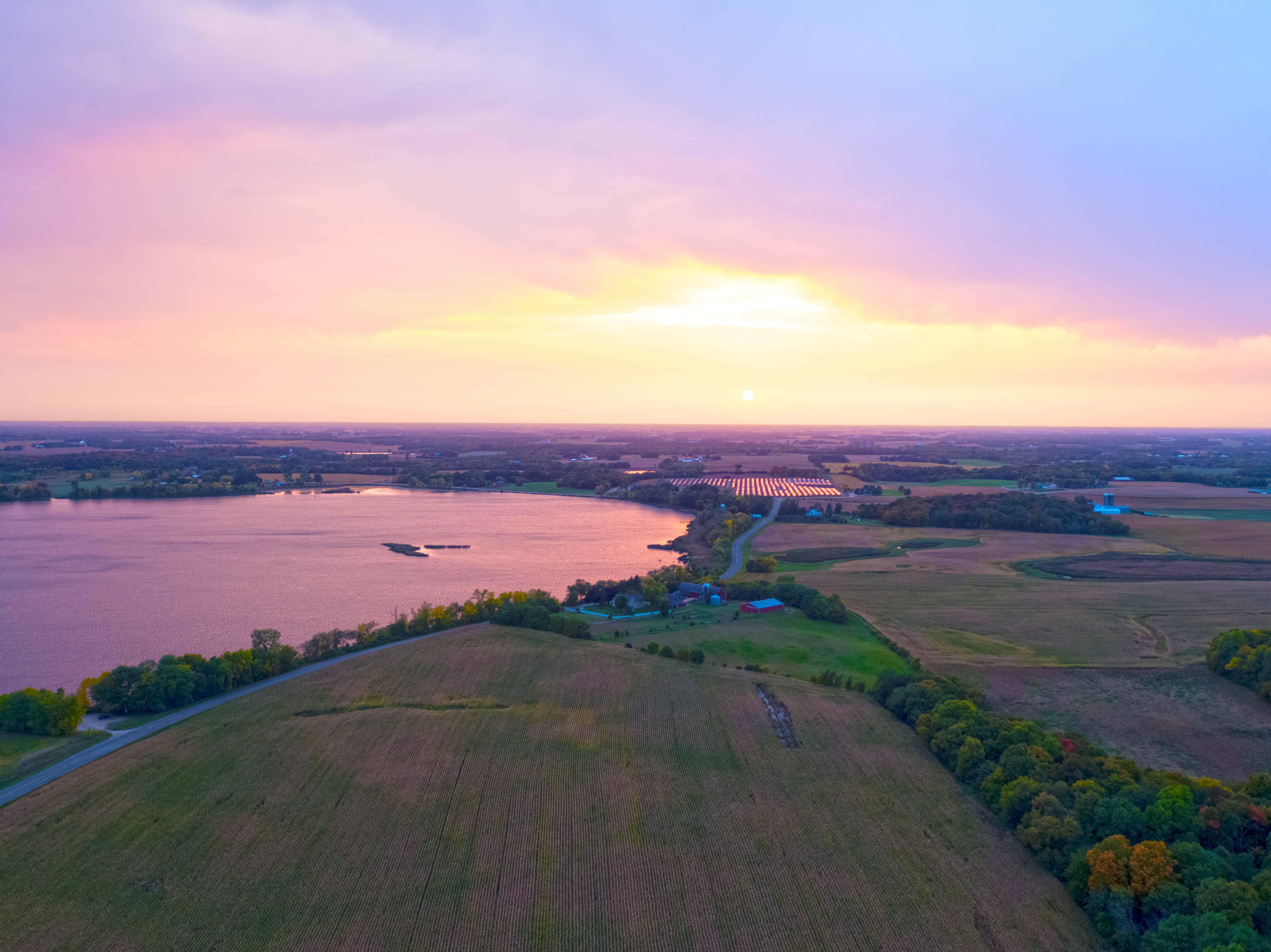 Inspirational aerial view of a sunset over a lake, farm, and solar farm.