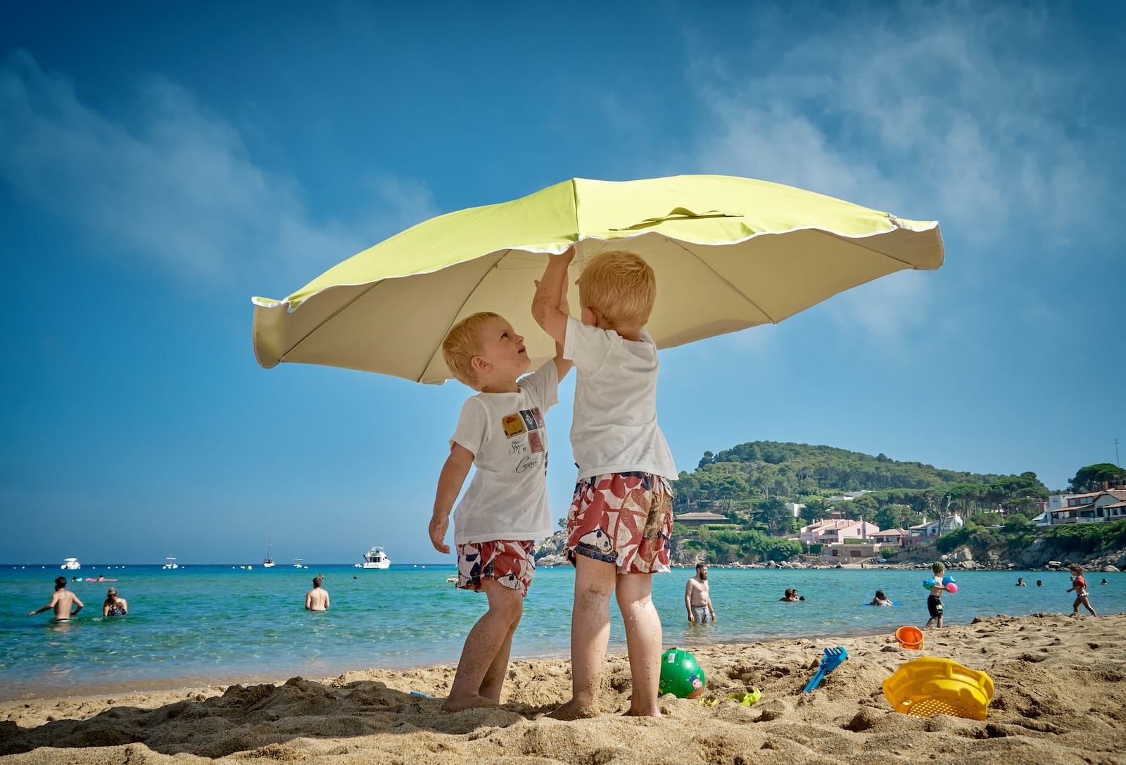 two children playing under umbrella on seashore-traveling with kids