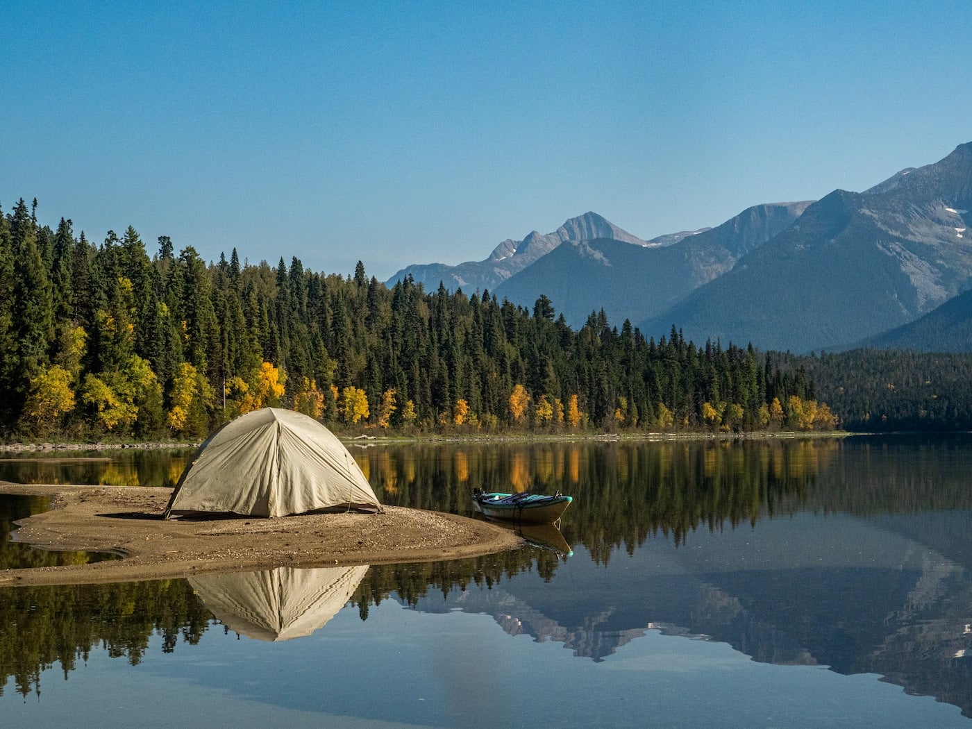 white tent on lake near green trees and mountain under blue sky during daytime-essential camping skills