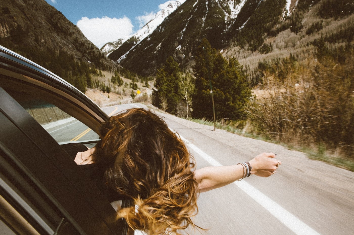 woman riding on vehicle putting her head and right arm outside the window while travelling the road-place plastic bag on car mirror when traveling alone