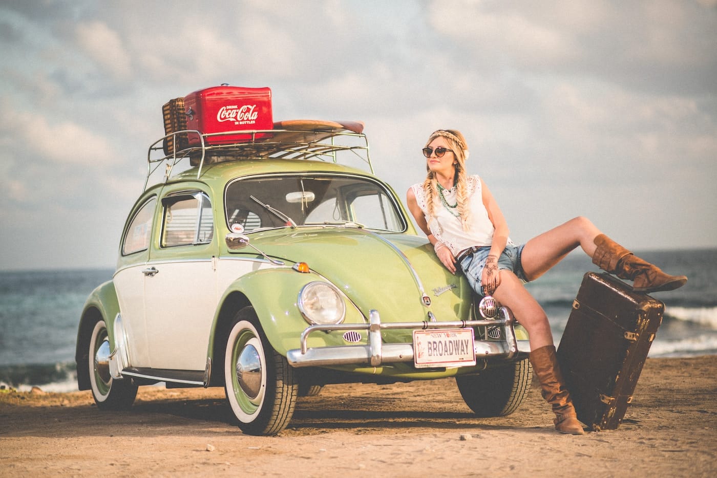 woman leaning on green and white Volkswagen Beetle near sea under white sky during daytime-How to Travel on a Budget in Your 20s