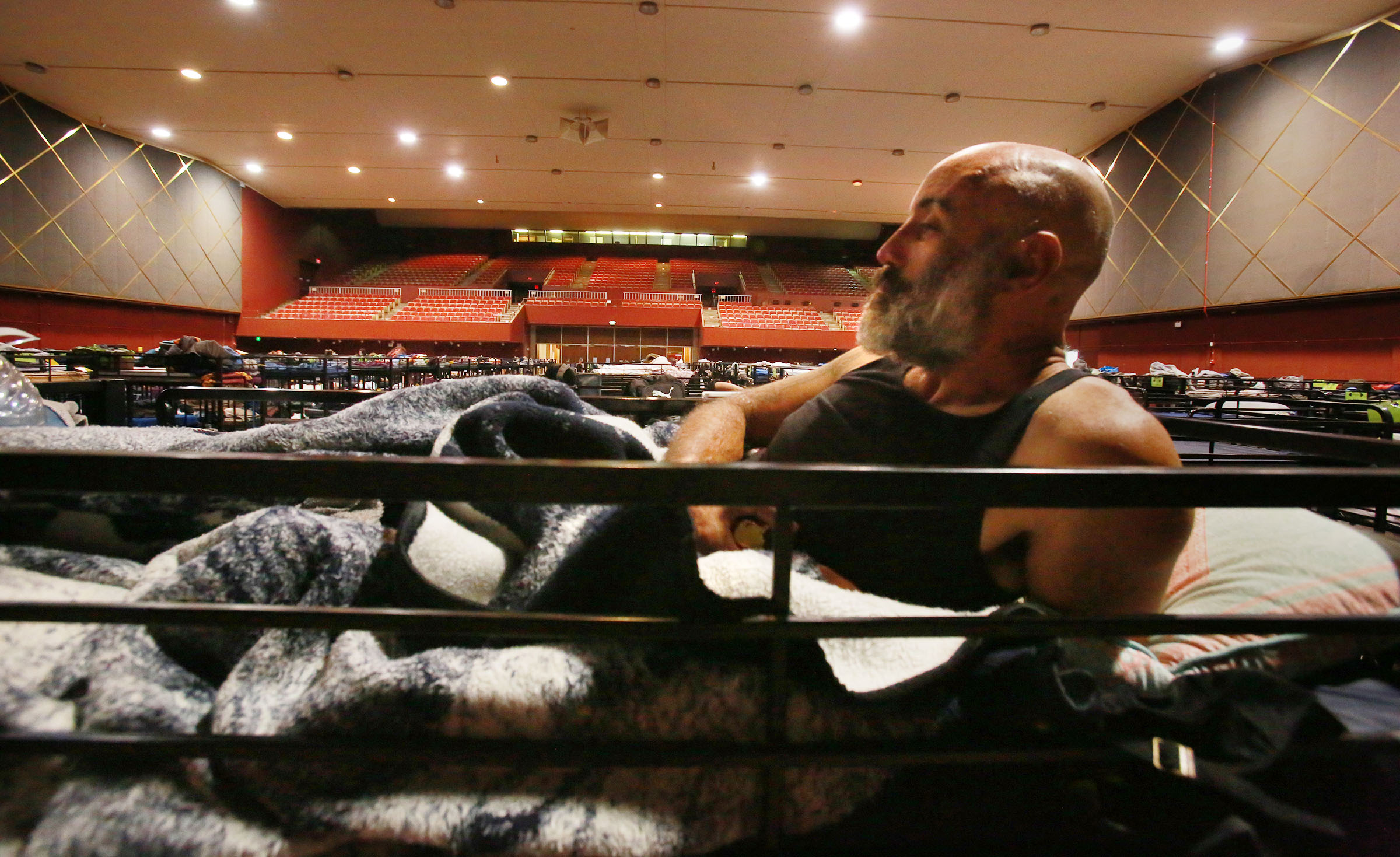 Ian Wiggill, 42, snacks on fruit in his upper bunk at the Golden Hall men’s shelter area on April 8, 2022. San Diego’s homeless shelters present a variety of opportunities for people experiencing homelessness, and an equal number of restrictions for residents there. The pandemic, rising housing costs, and competition for low-income housing all conspire to put the focus on how to house the growing number of people who fall through the cracks. / Photo by Peggy Peattie for Voice of San Diego