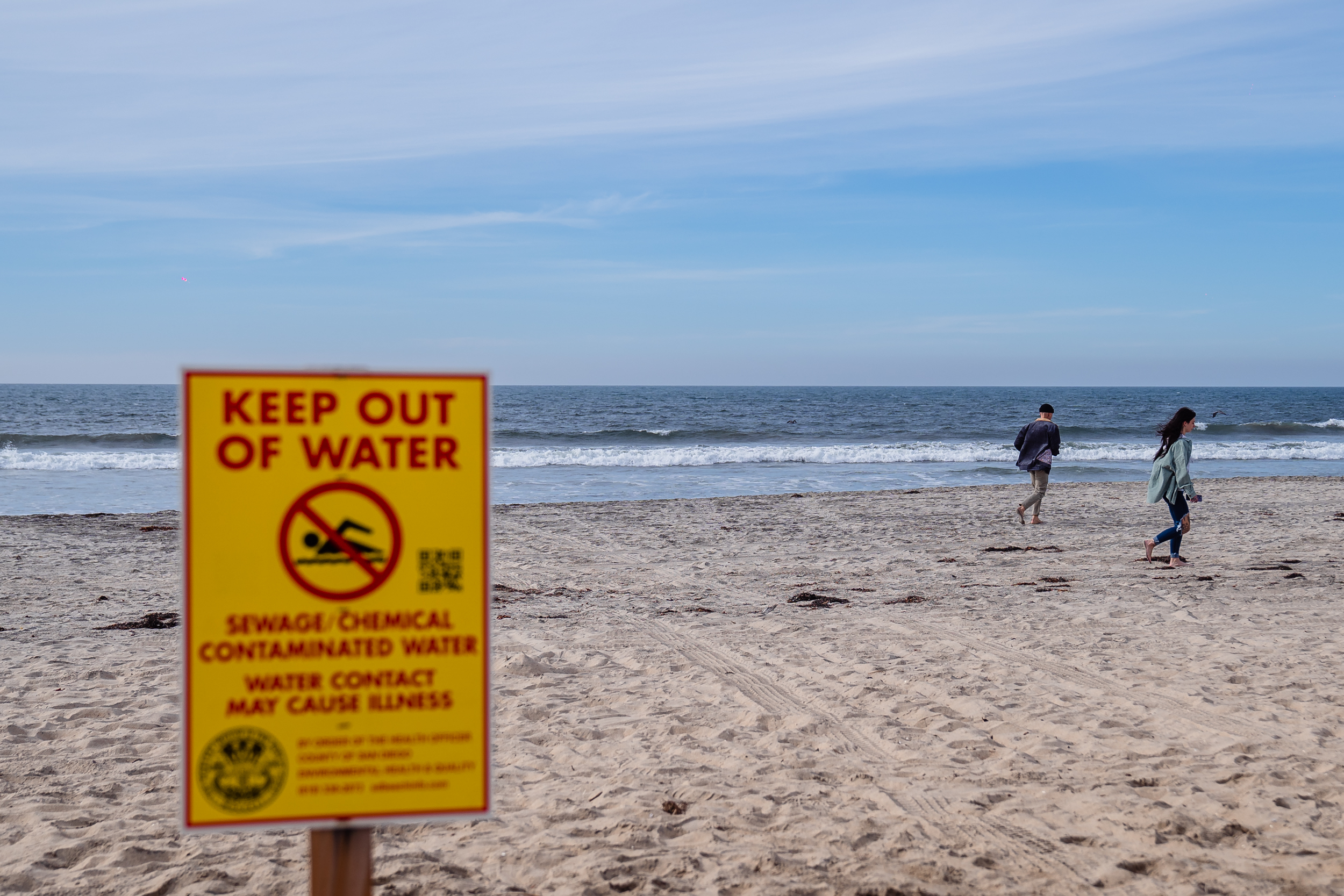 People walk near the "Keep Out Of Water" sign in Imperial Beach on Dec. 4, 2023.