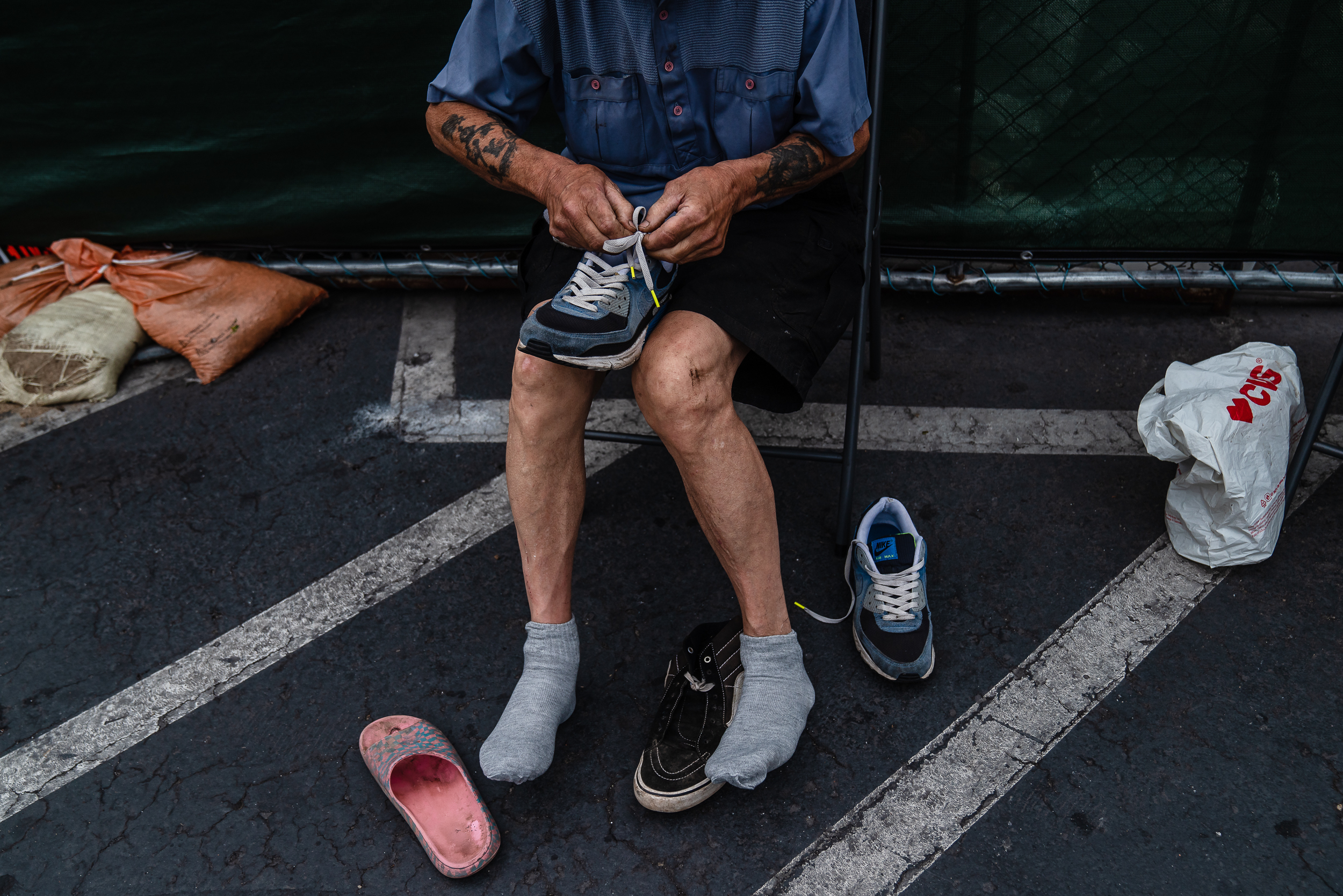 James Gillinger, 73, changes shoes in front of the Alpha Project shelter in the Midway District on July 17, 2024. Gillinger's feet hurt from walking and Alpha Project’s Homeless Outreach Supervisor Craig Thomas gave him a different pair of shoes. / Ariana Drehsler for Voice of San Diego