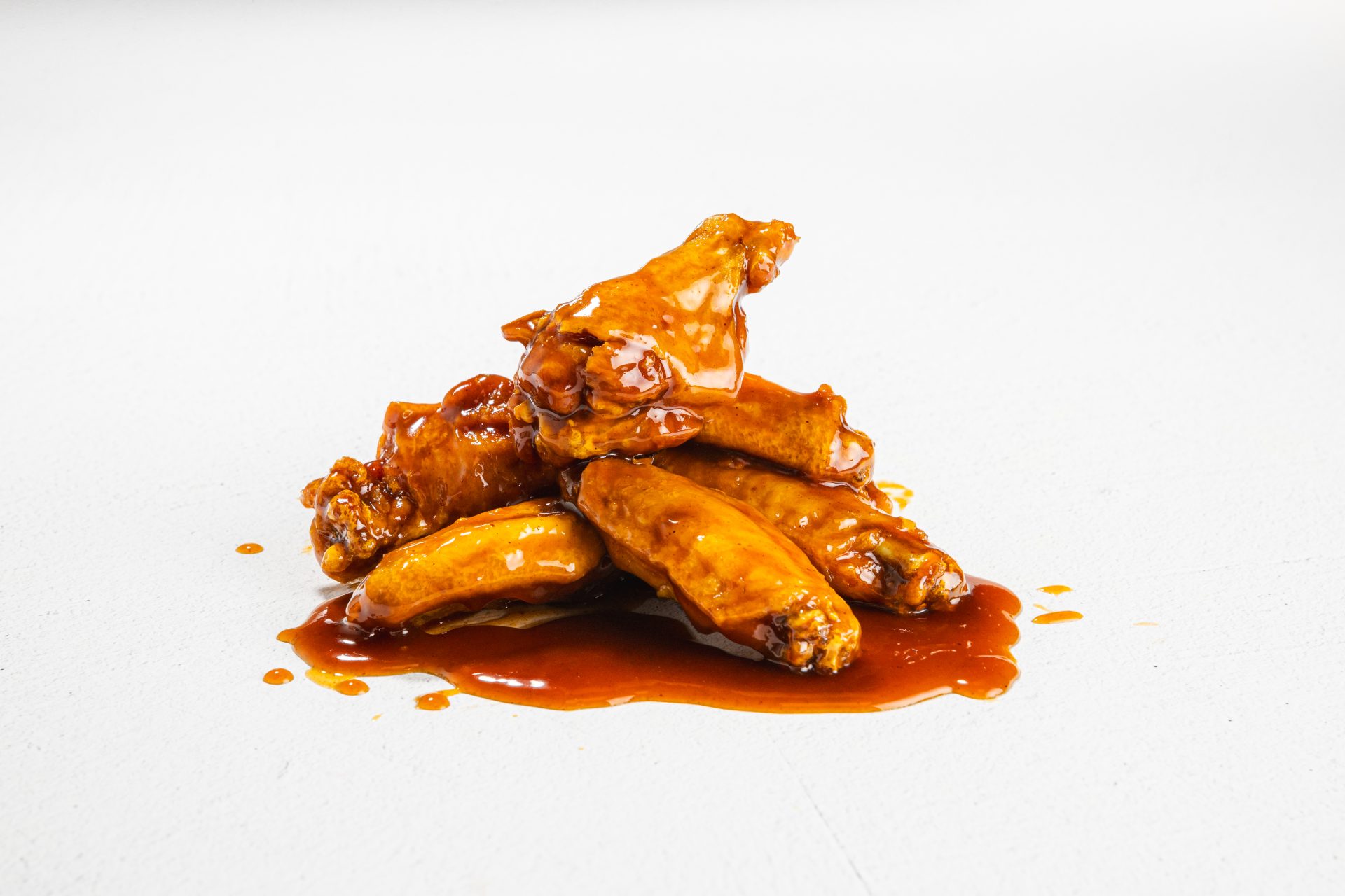 Plump, juicy chicken wings drenched in a rich, spicy brown buffalo sauce. The wings are glossy with the sauce, which has a perfect balance of heat and flavor, making them look irresistibly delicious. They are served on a plate, ready to be devoured with a side of cool dipping sauce.