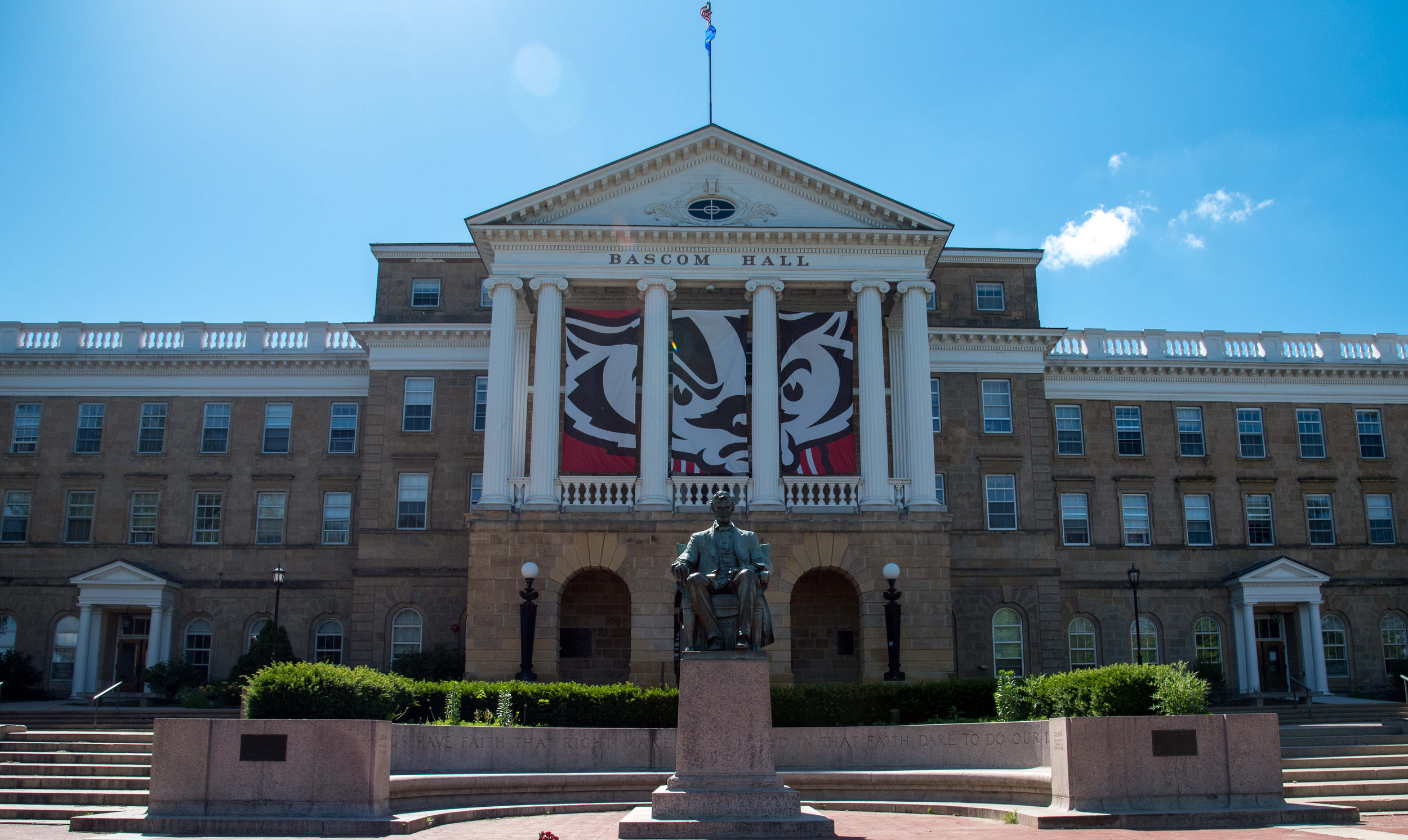 A statue of U.S. President Abraham Lincoln sits in front of Bascom Hall on the University of Wisconsin-Madison campus under a blue sky.
