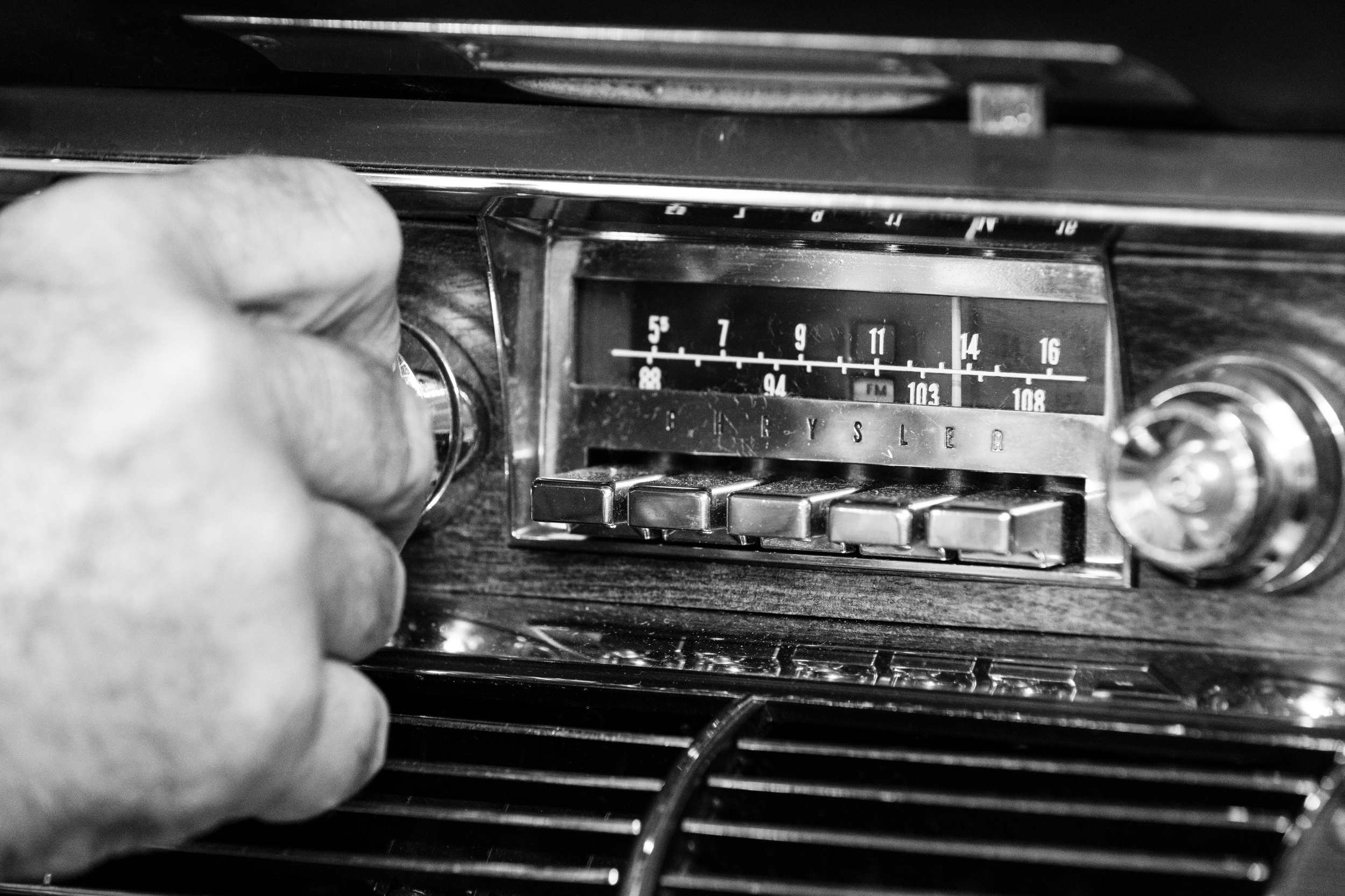 A hand adjusts a dial on an old car radio.