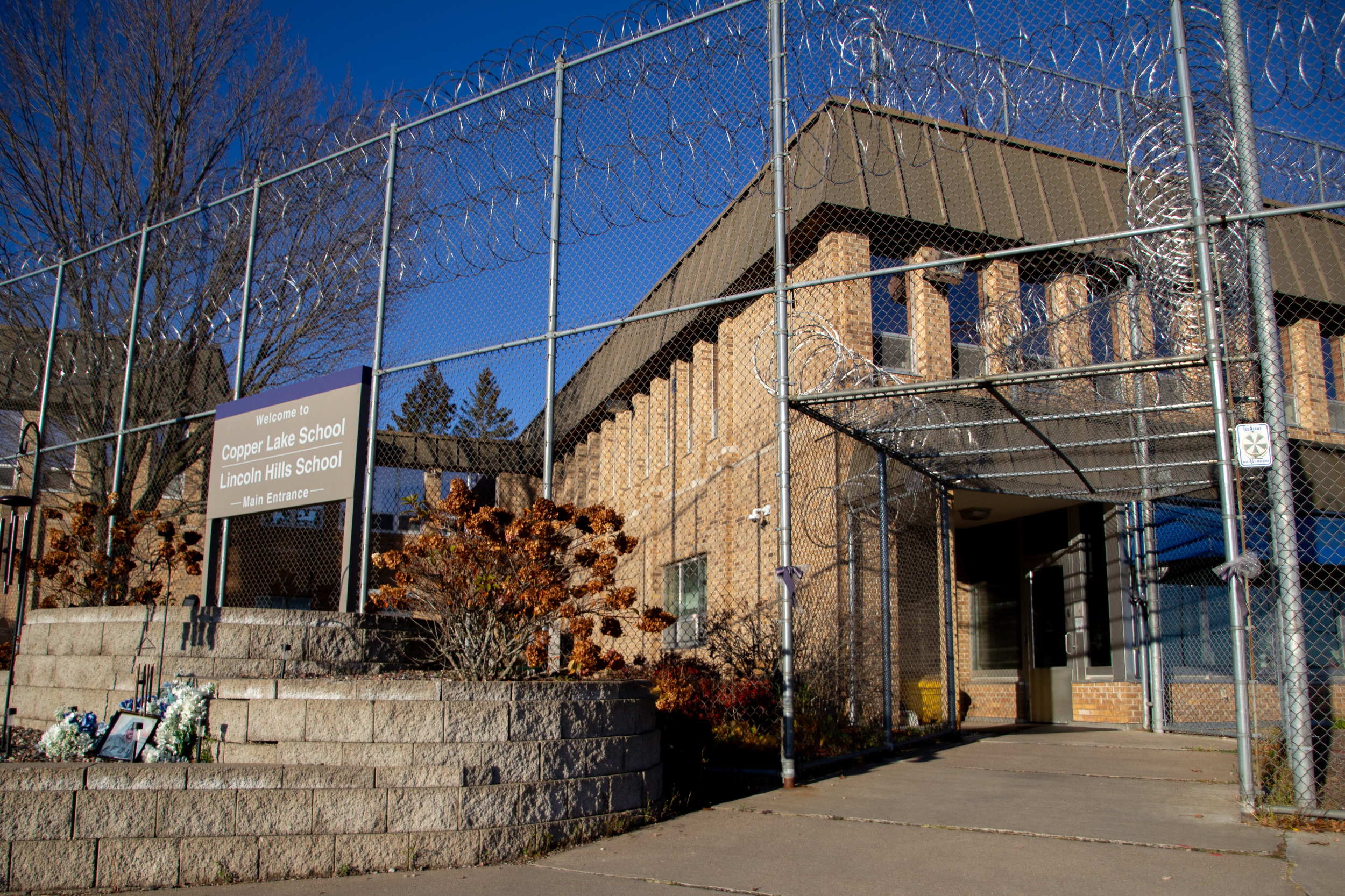 Exterior view of building and metal fence with barbed wire. Sign says “Welcome to Copper Lake School Lincoln Hills School”
