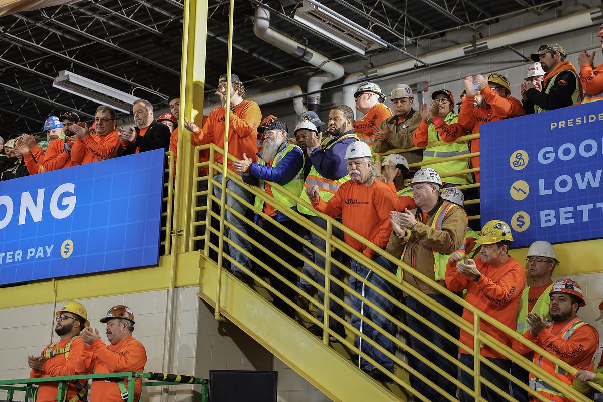 Workers in hard hats and yellow and orange vests clap inside a building