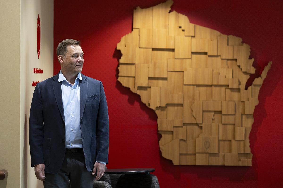 Man stands next to wall art piece in the shape of Wisconsin.