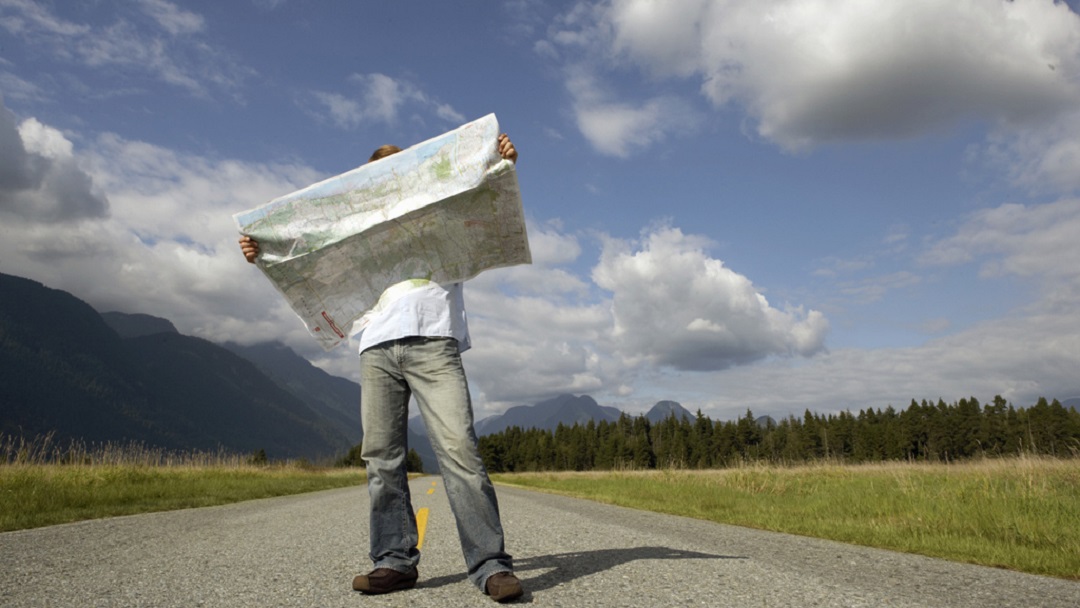 Man with ADHD standing on road holding map with mountains behind him