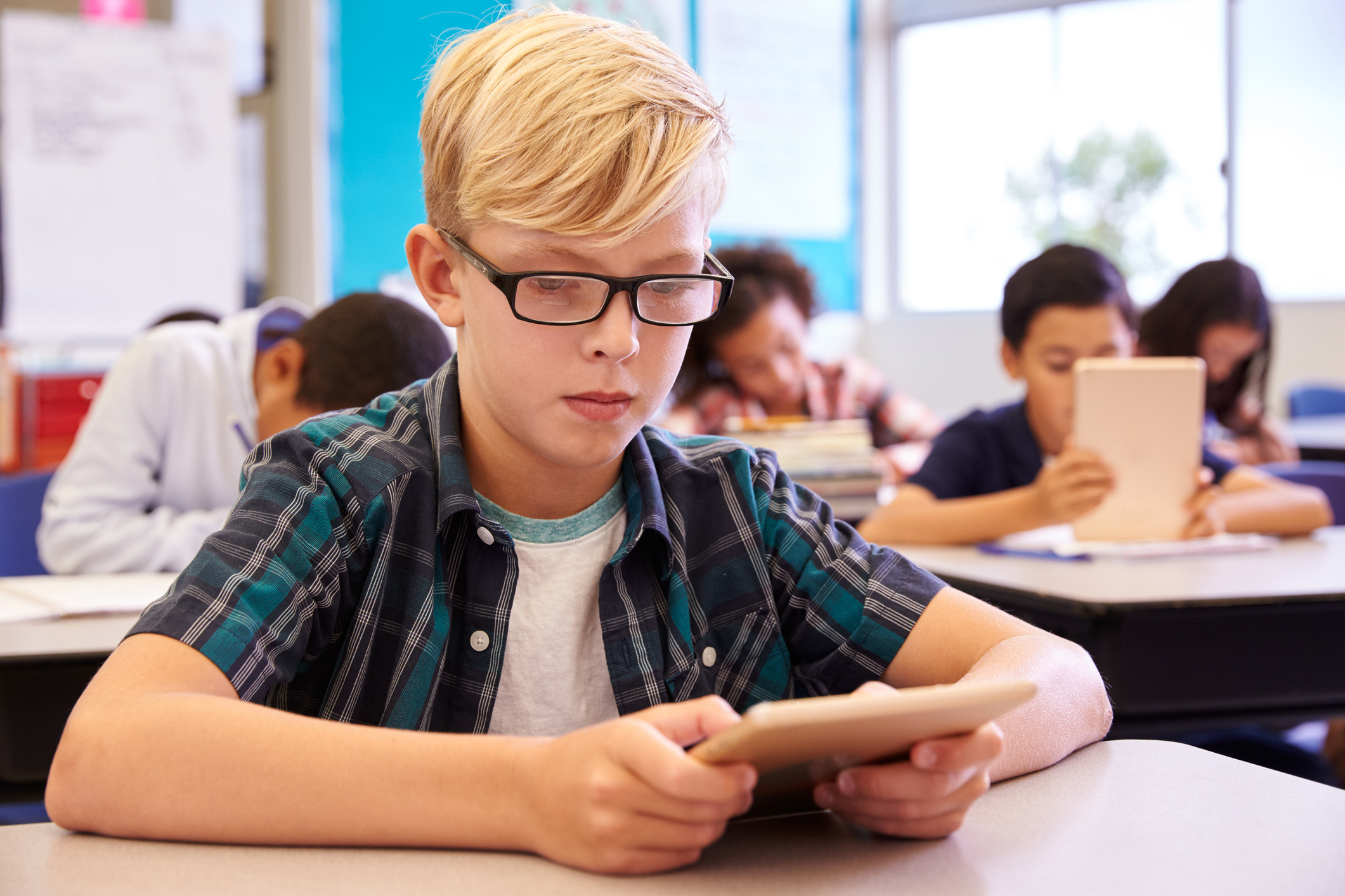 Boy with ADHD wearing glasses using tablet in elementary school class