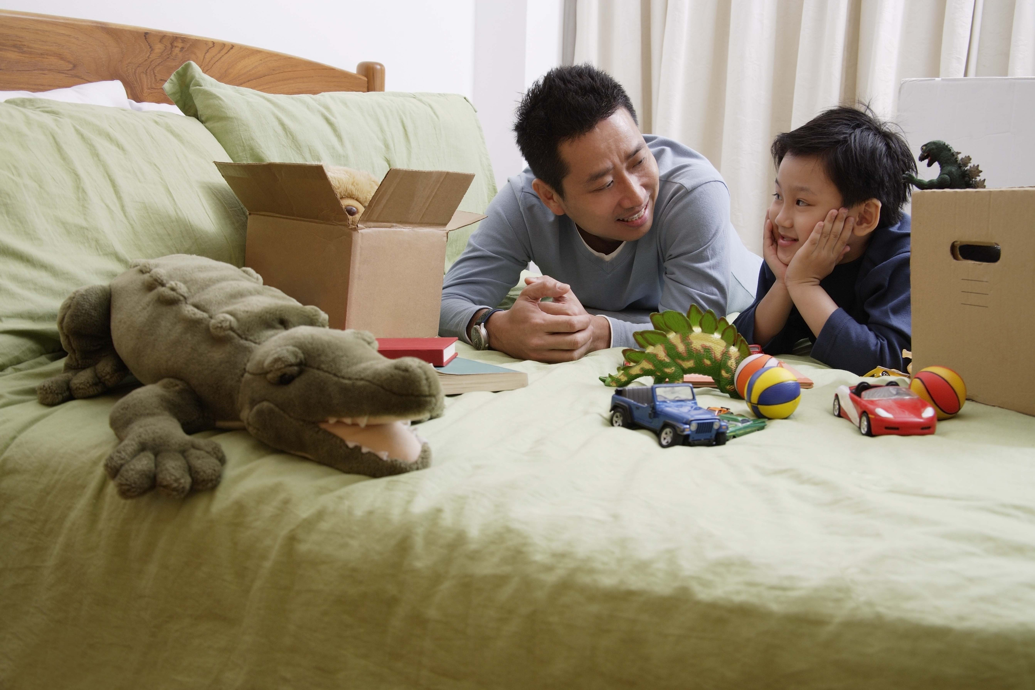 A dad helps his son with ADHD put toys in a box to clean up his messy bedroom.