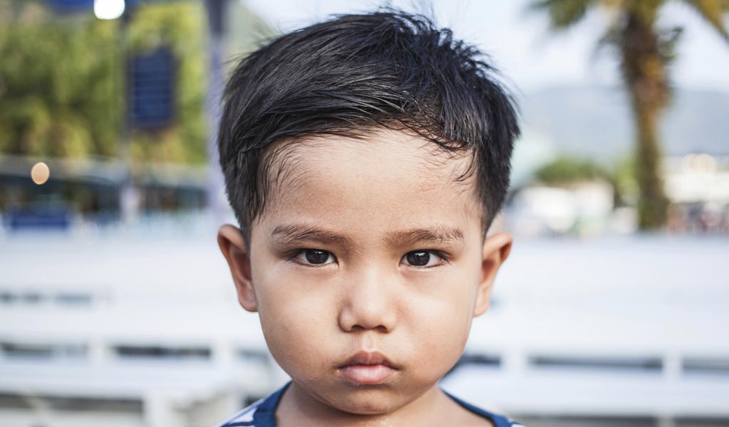 Sad little boy with ADHD frowning into camera