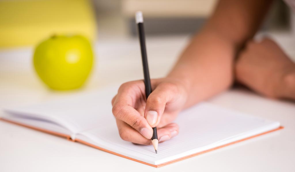 Girl with ADHD writing in notebook with apple beside her trying to prepare for class