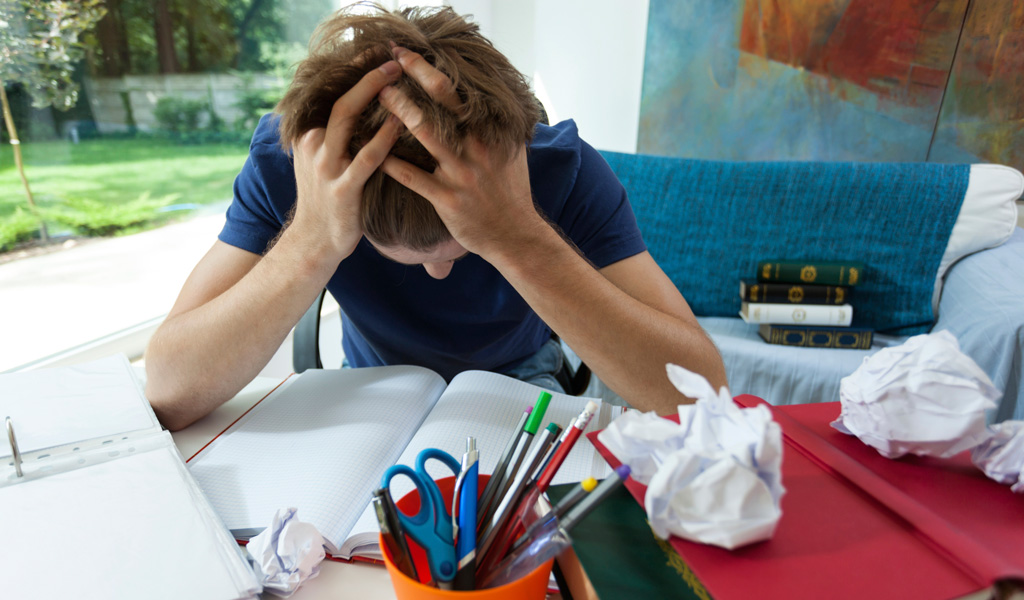 ADHD student with head in hands surrounded by books and paper overwhelmed by disorganization in room