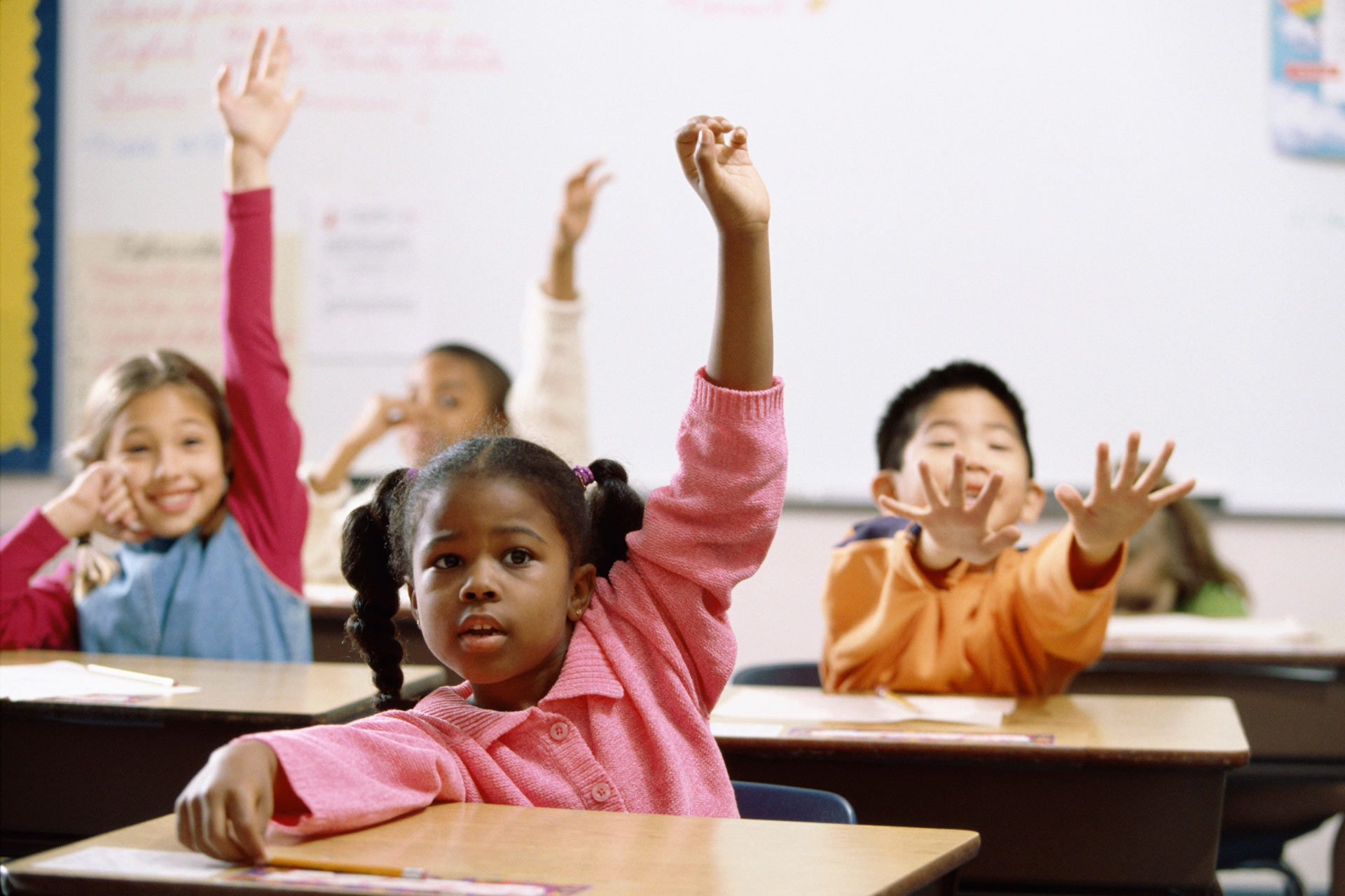 Children raising their hands in a classroom, following the rules for answering a question