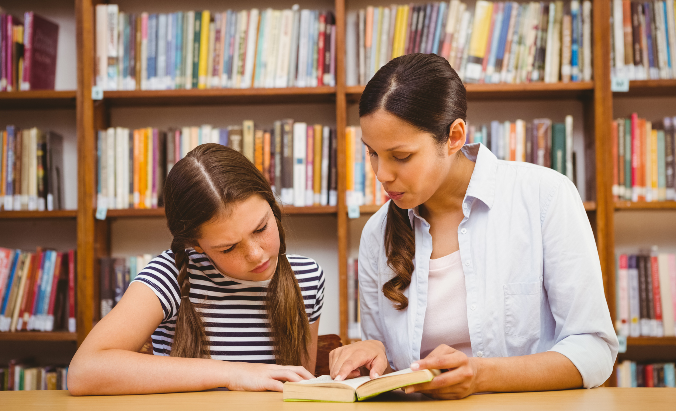 A young girl with ADHD and her tutor working in the library