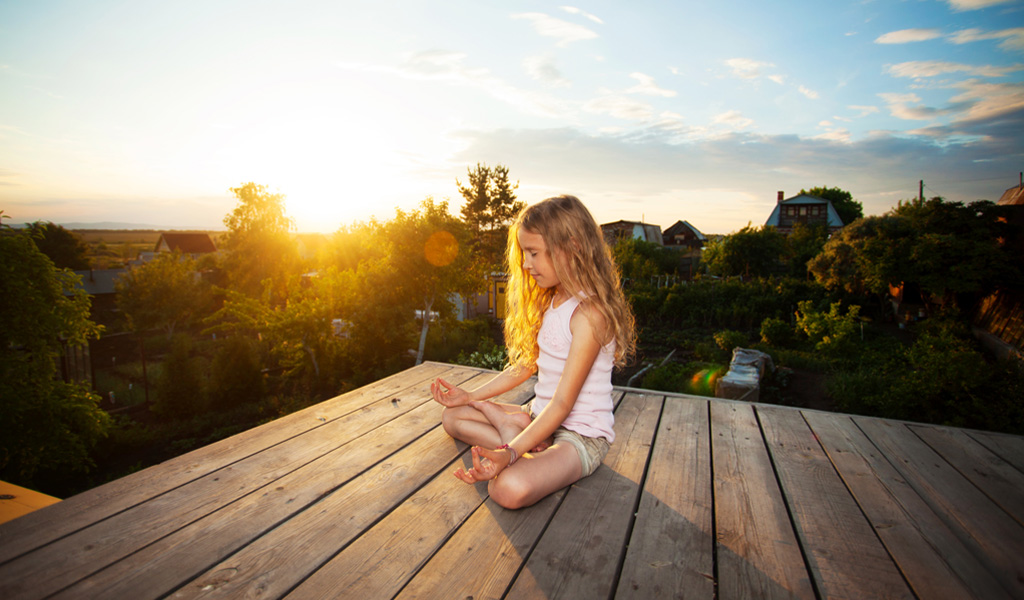 Girl with ADHD meditating outside on porch at sunset.