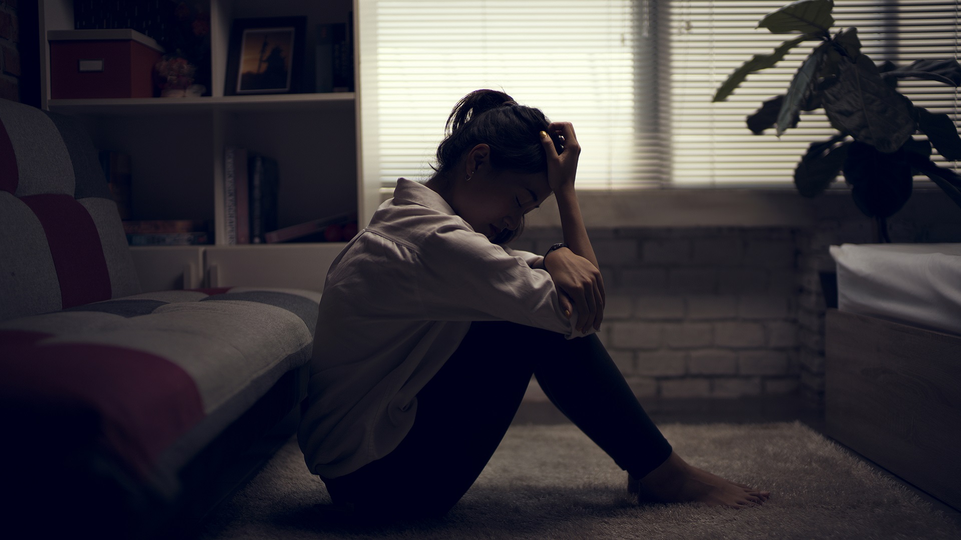 A woman with depression sits in a darkened room.