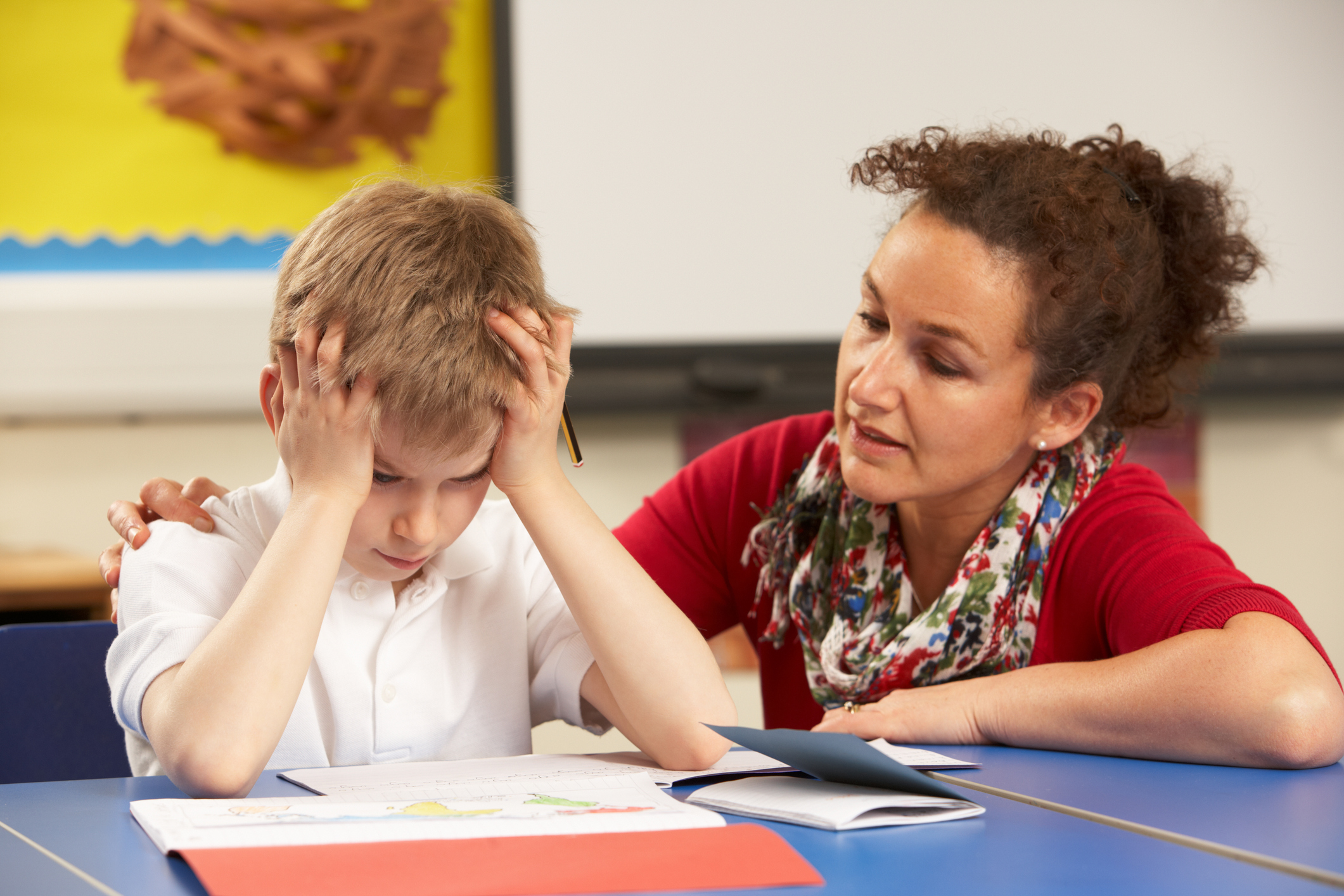 Stressed ADHD Schoolboy Studying In Classroom With Teacher
