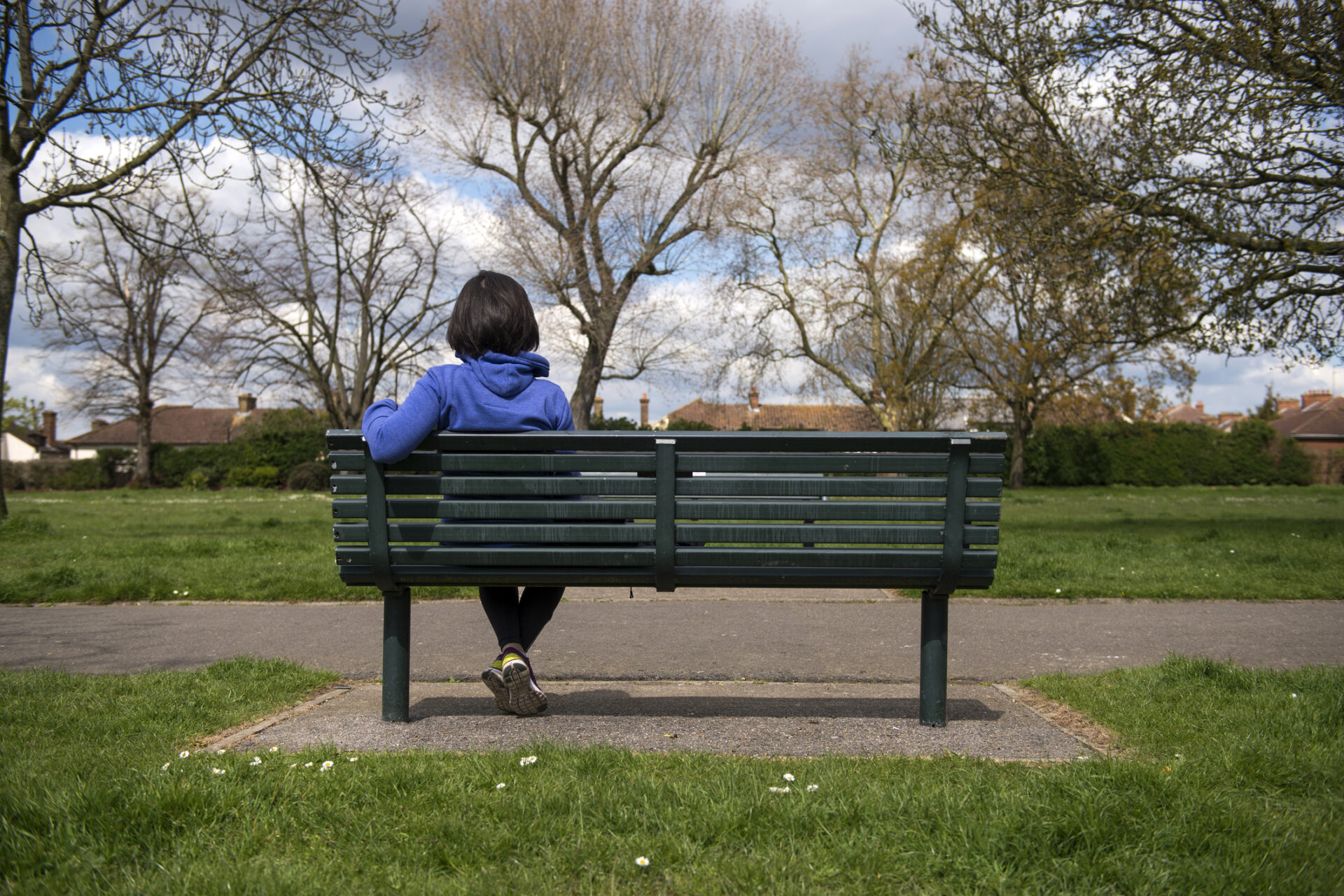 ADHD Woman sitting on bench with back turned looking at the park thinking