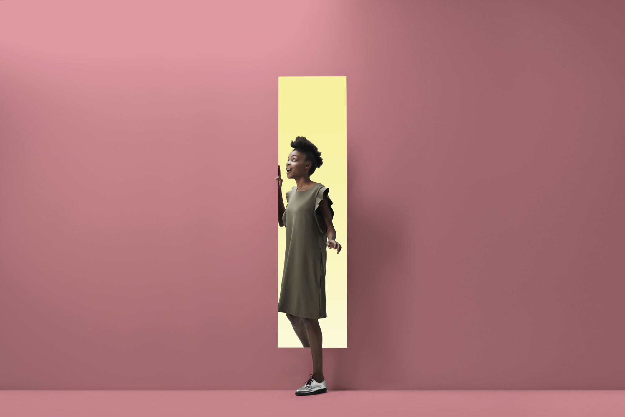 Woman walking out of rectangular opening of coloured wall