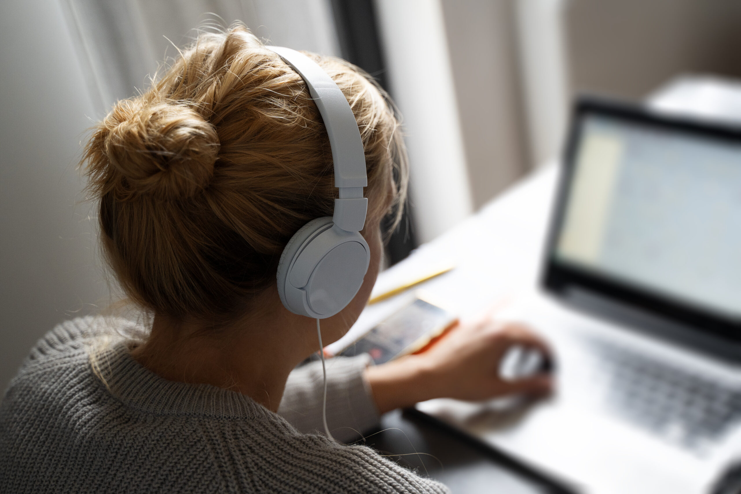 Blonde woman with headphones working on notebook computer.