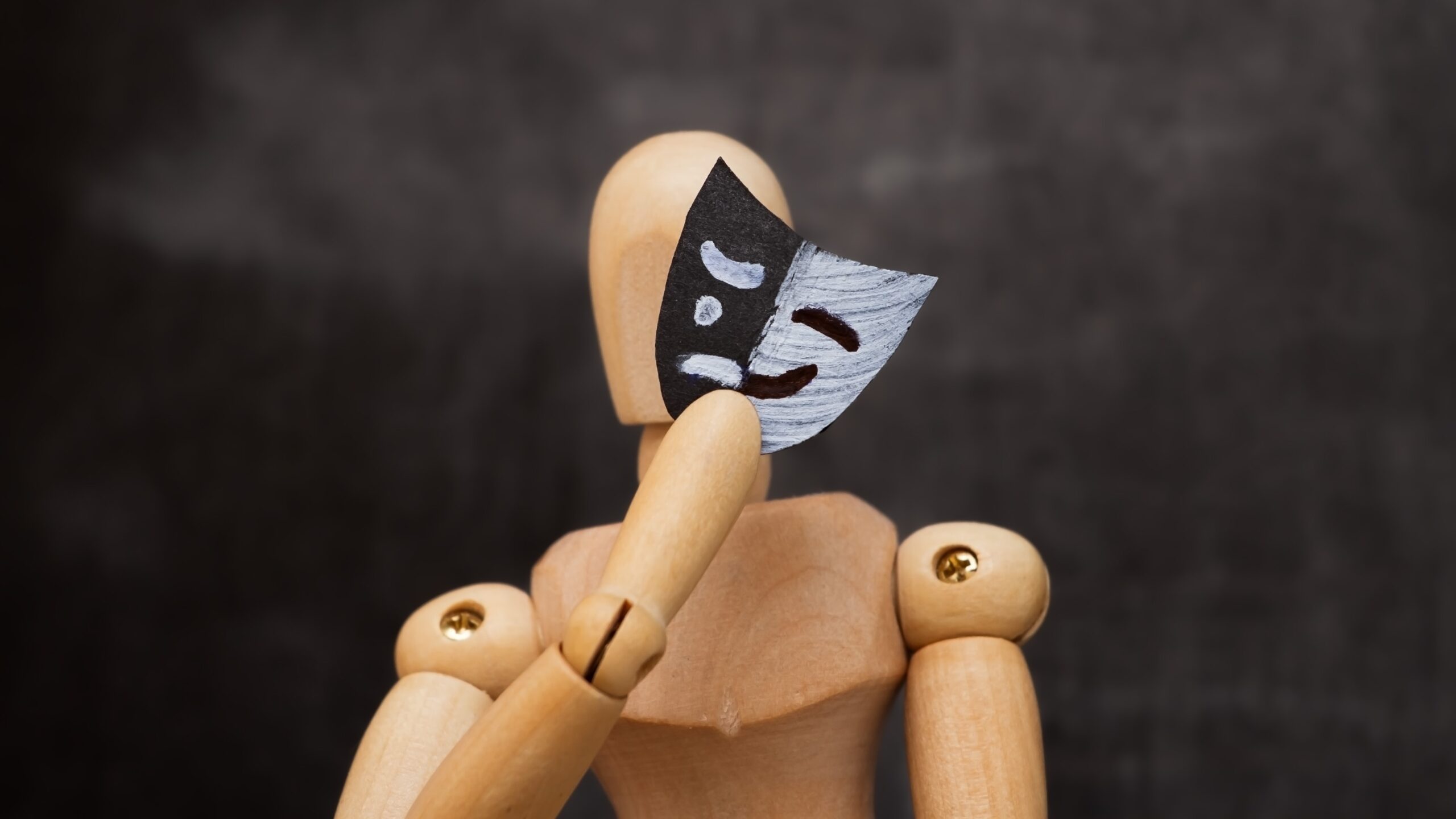 Imposter syndrome concept image: A wooden figure holding a mask over its face.