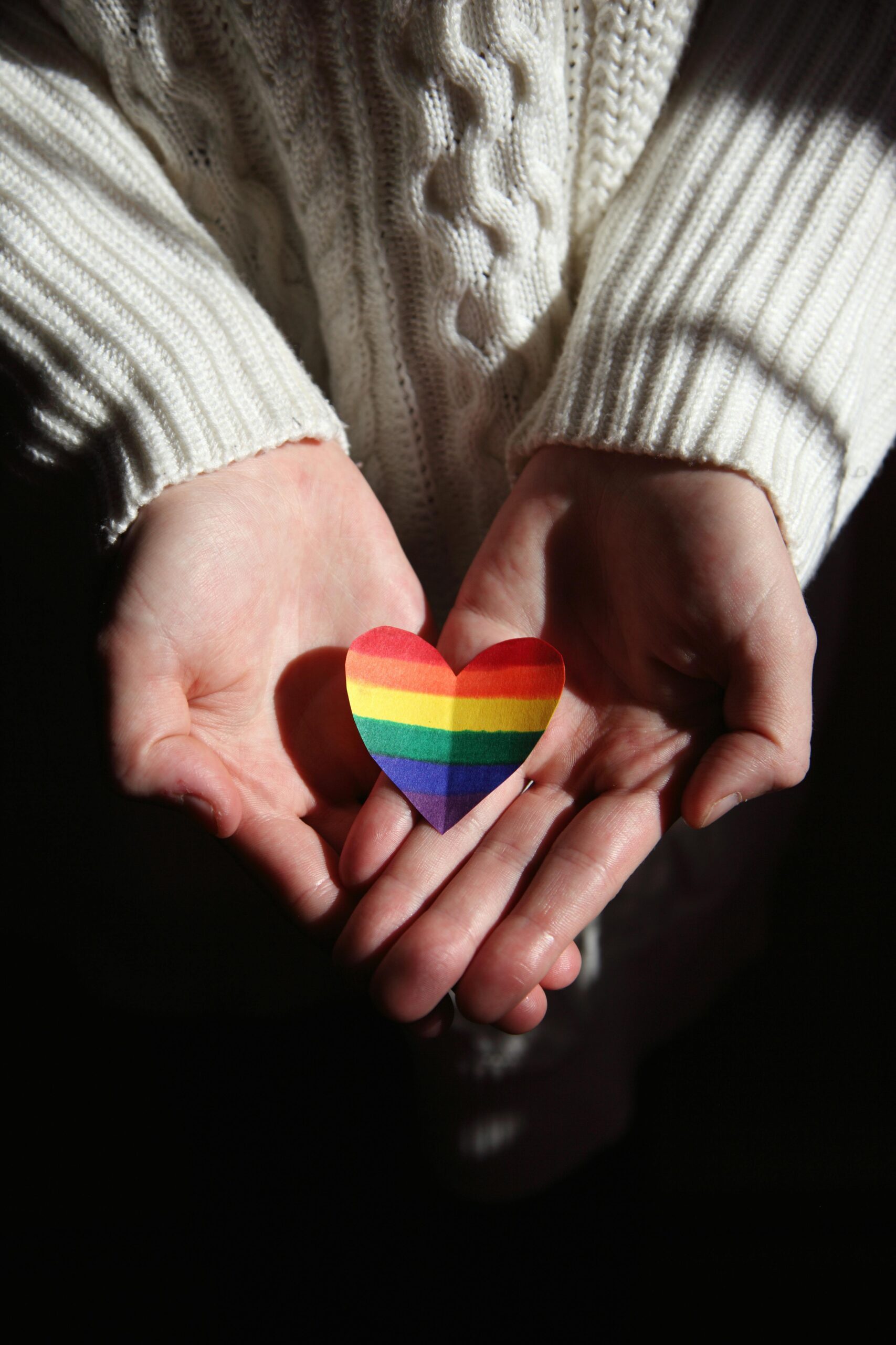 Rainbow pride heart placed in the palms of two hands.