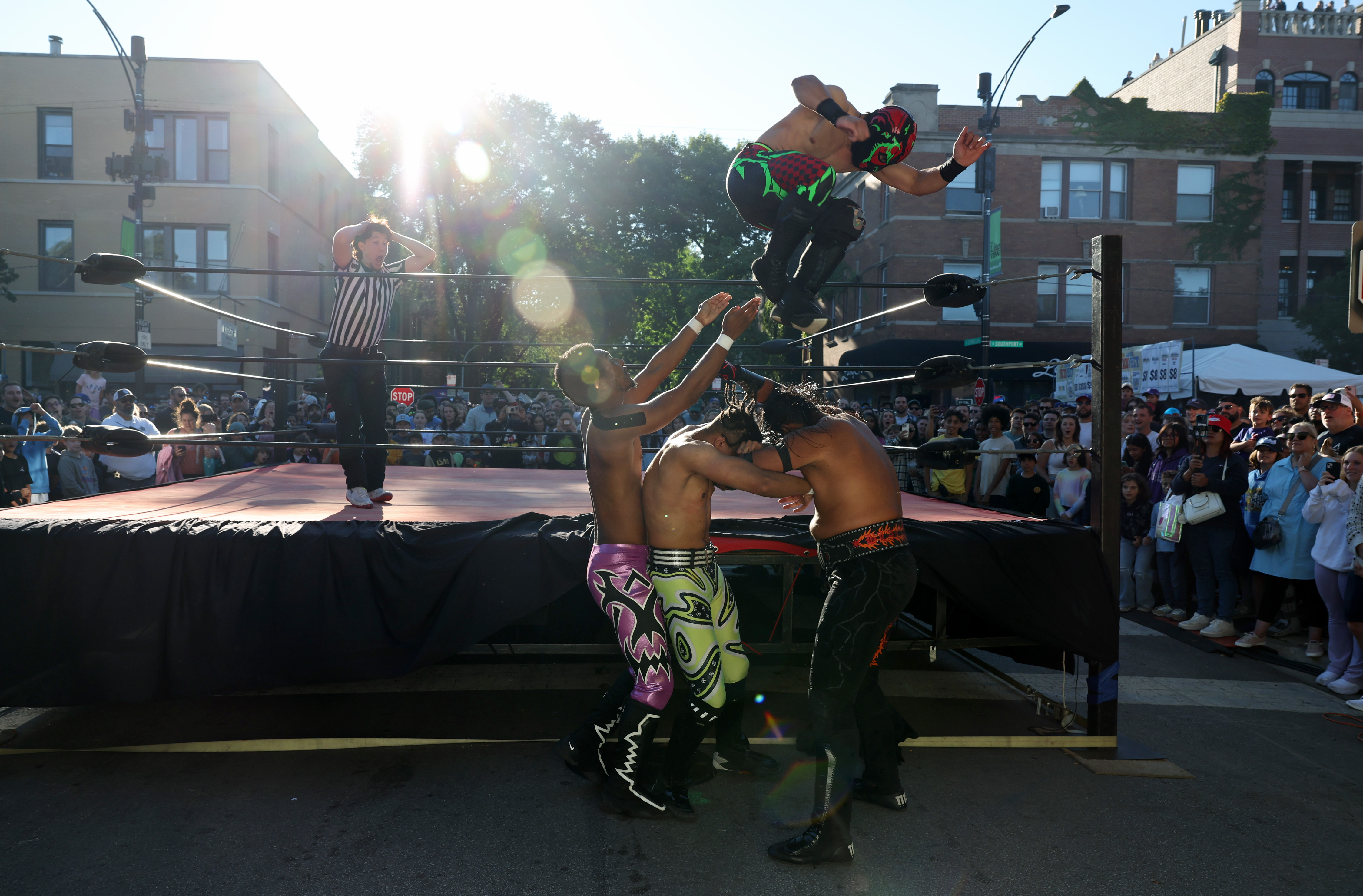 "Lizard Man" jumps onto three others outside the ring during a Lucha Libre Mexican professional wrestling tag team event at the Lakeview Taco Fest in the 3500 block of North Southport Avenue on Saturday, Sept. 7, 2024, in Chicago. (John J. Kim/Chicago Tribune)