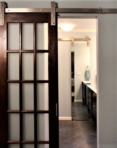 Barn doors are often overused in Modern Farmhouse style. I like to use them where they make sense in the floor plan, not gratuitously. Replacing a swing door with a barn door as the entry to the master bath in this renovation provided the extra square footage needed to fulfill the clients' wish for two separate vanities. For storage, we built an alcove into the wall using a mirror on barn door hardware. (Sharon McCormick Designs, Brian Urso Photography)
