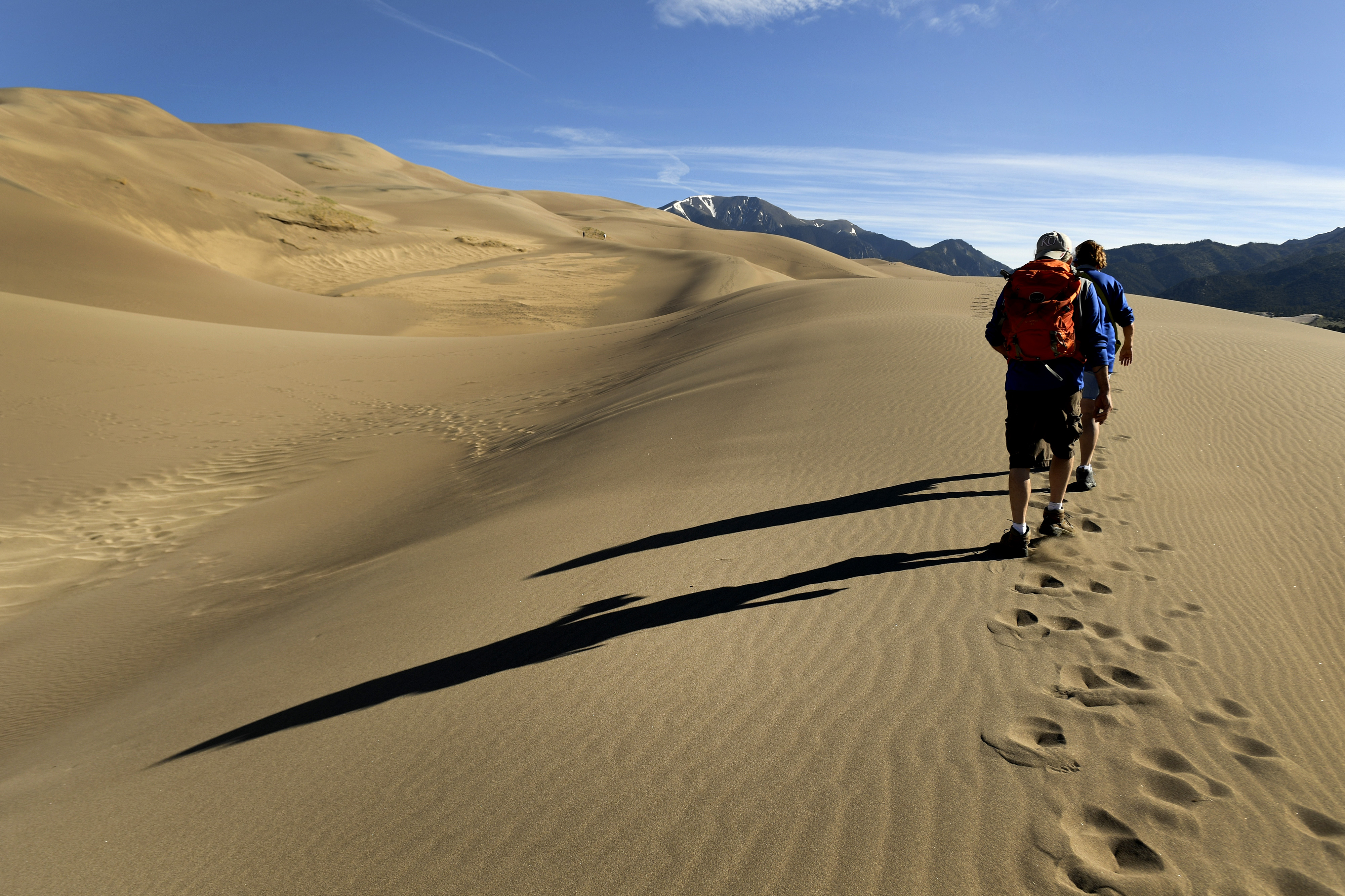 MOSCA, CO - JUNE 20: Hikers Tara Eisenhour, in front, and Jim Smith, in back, make their way towards the top of the dunes at the Great Sand Dunes on June 20, 2019 in Mosca, Colorado. Great Sand Dunes National Park and Preserve is known for huge dunes like the towering Star Dune, and for the seasonal Medano Creek and beach created at the base of the dunes. These sand dunes are the tallest dunes in North America. They are shaped by the forces of wind and water and are continuously moving and shifting. The dunes comprise 30 square miles of dunes, 750 ft elevation gains and average hike times to the top of the dunes is 2 hours. Also in the area is the backcountry Medano Pass Primitive Road winds through a canyon toward the Sangre de Cristo mountains. Trails lead to forests, wetlands and alpine lakes like Medano Lake, which is home to trout and tundra wildlife. (Photo by Helen H. Richardson/The Denver Post)