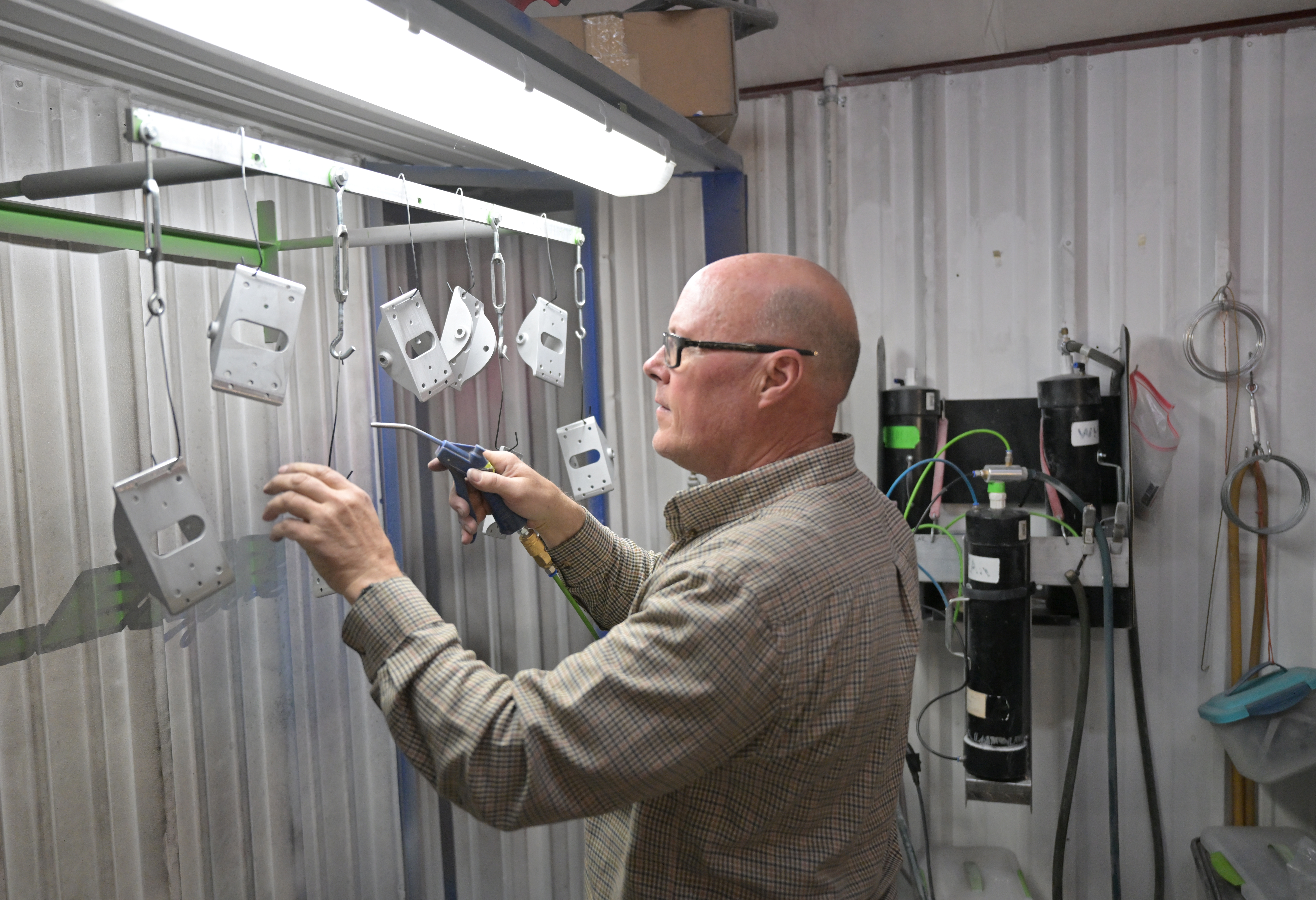 Devin Lenz gets ready to do a powder coating on parts for ski bikes this week in his shop in Fort Lupton. Color coating comes out of a spray gun with a positive charge. The pieces to be colored are electrically grounded on the spray rack, helping the coating bind to the piece. (RJ Sangosti/The Denver Post)