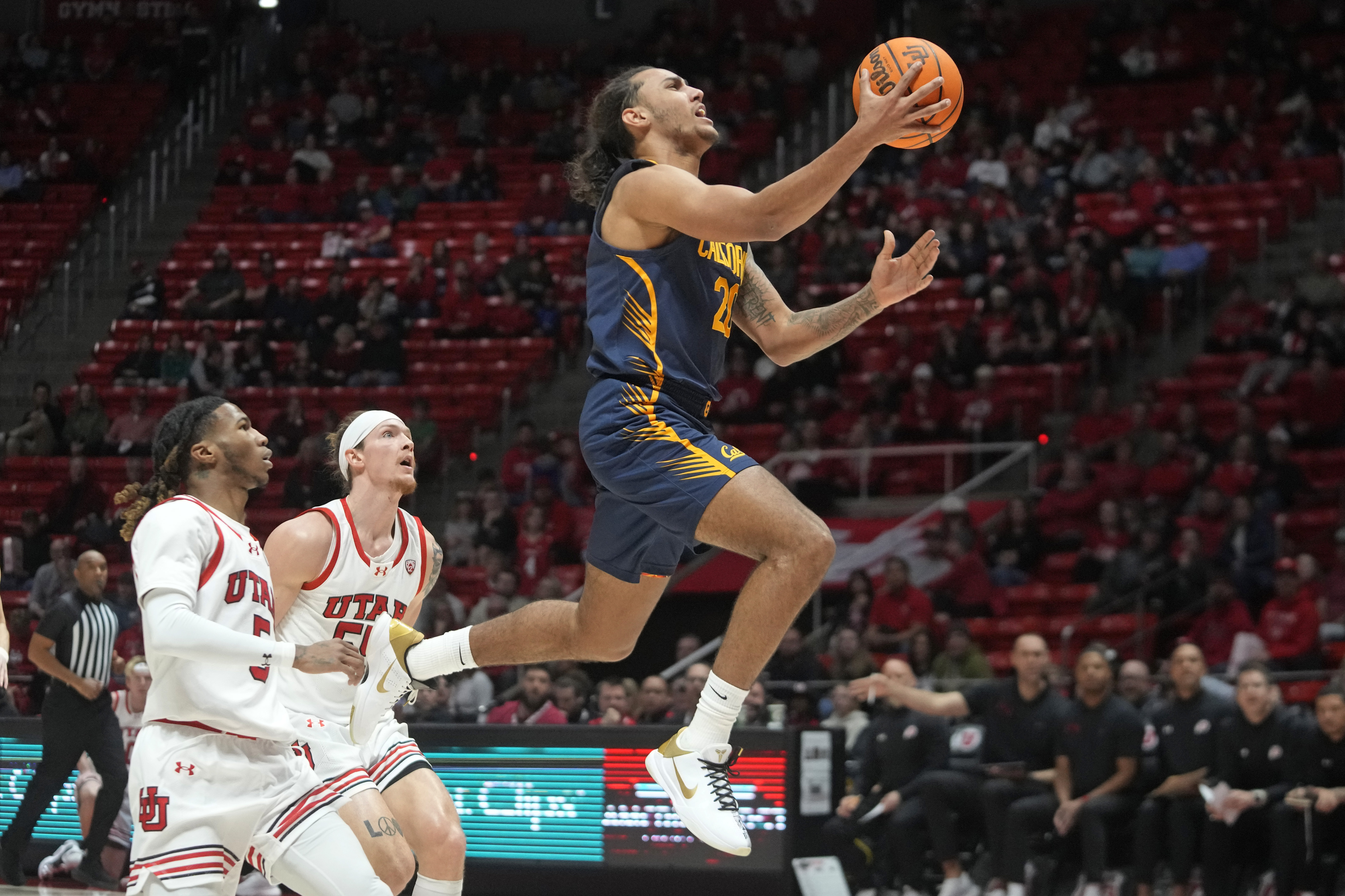 California guard Jaylon Tyson (20) goes to the basket as Utah's Deivon Smith, left, and Gabe Madsen defend during the first half of an NCAA college basketball game Saturday, March 2, 2024, in Salt Lake City. (AP Photo/Rick Bowmer)