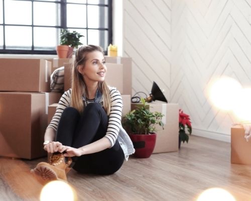 a young woman sitting on the floor with moving boxes by her, smiling