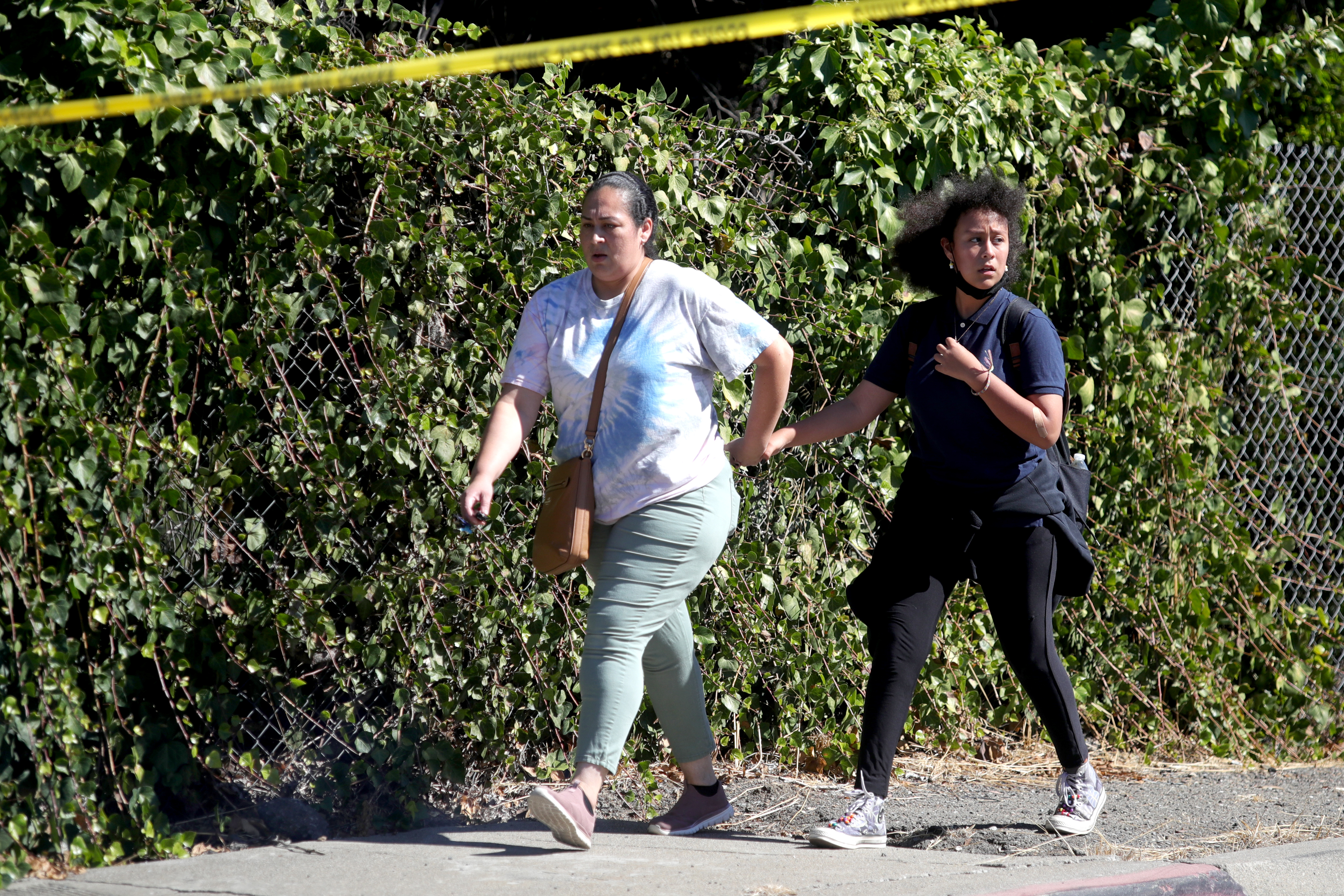 OAKLAND, CALIFORNIA - SEPTEMBER 28: A woman with a kid walk along Fontaine Street in Oakland, Calif., after a multiple people were shot in a complex of schools on Wednesday, Sept. 28, 2022. Ray Chavez/Bay Area News Group)